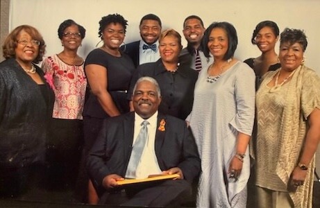 Elderly man in a suit seated center, surrounded by smiling colleagues at a formal group photo.