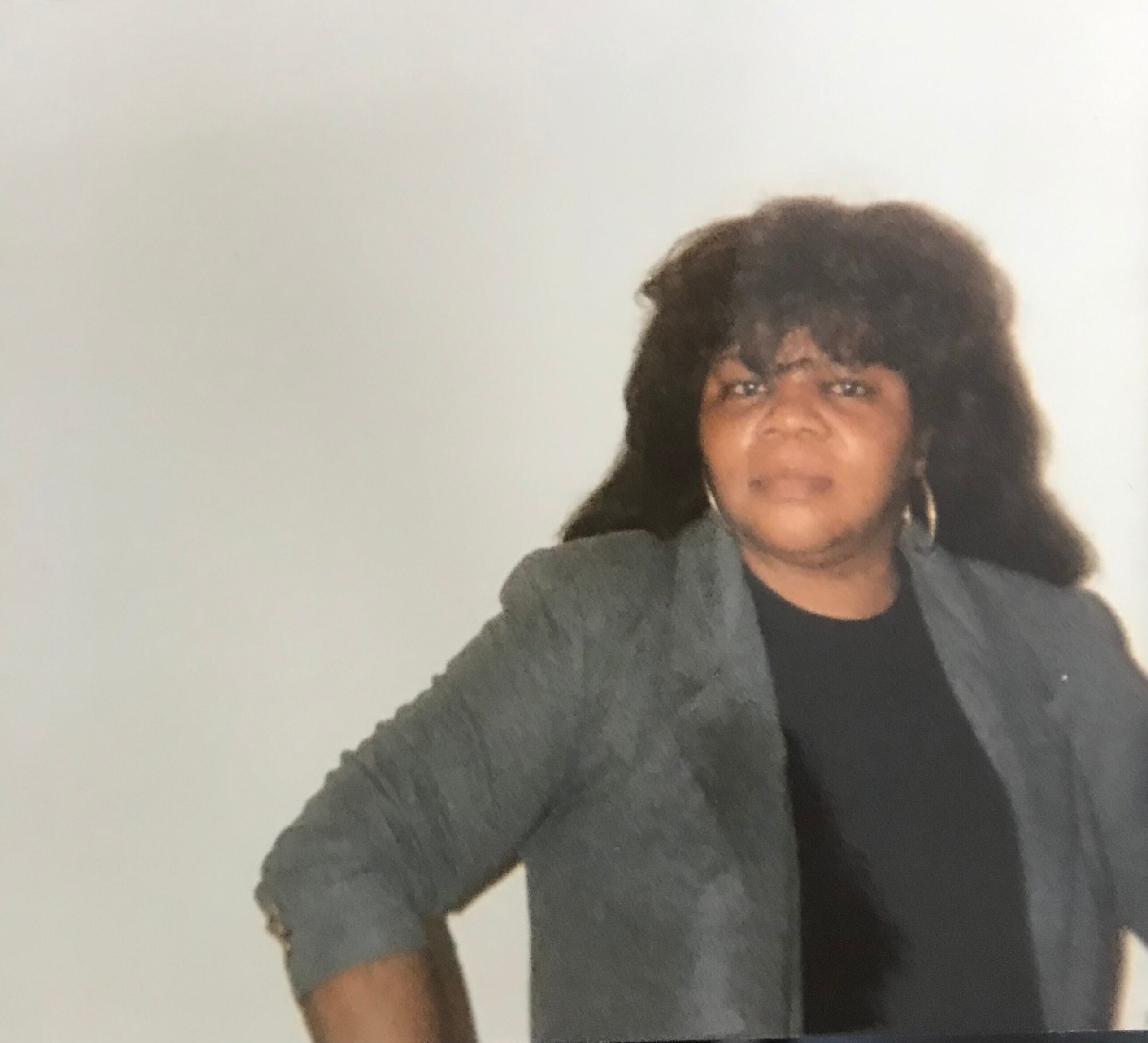 Person wearing a gray blazer over a black top, posing against a pale background.