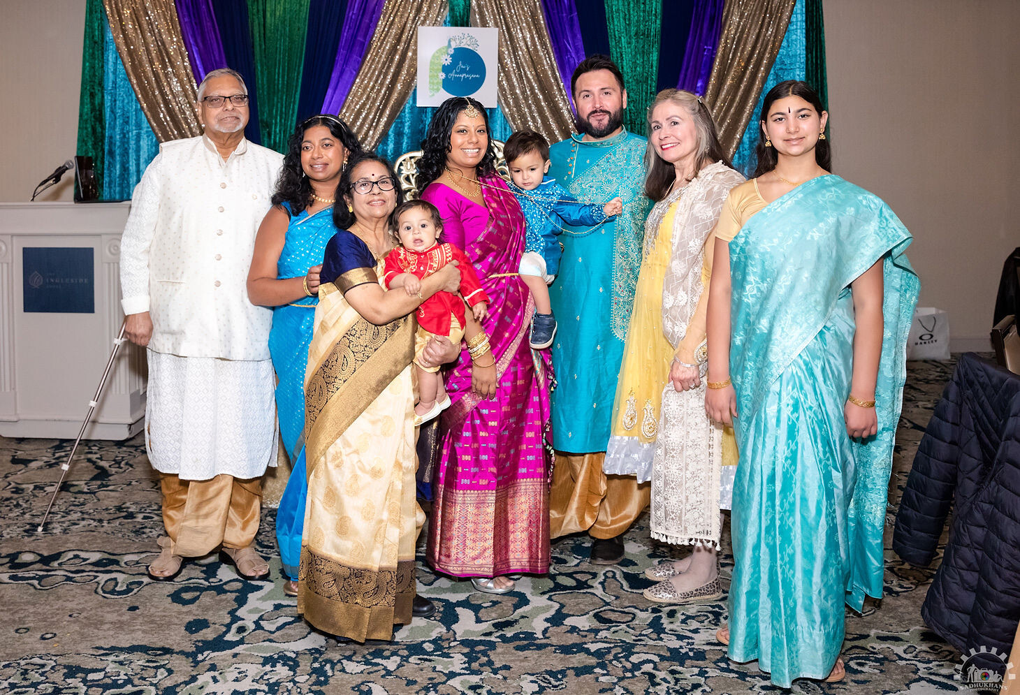 Group of Indian family members in bright saris and sherwanis posing for a photo at a celebration.