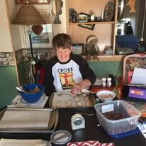 Boy at a crafts/kitchen table, cutting or preparing items with bowls and trays around him in a workshop setting.