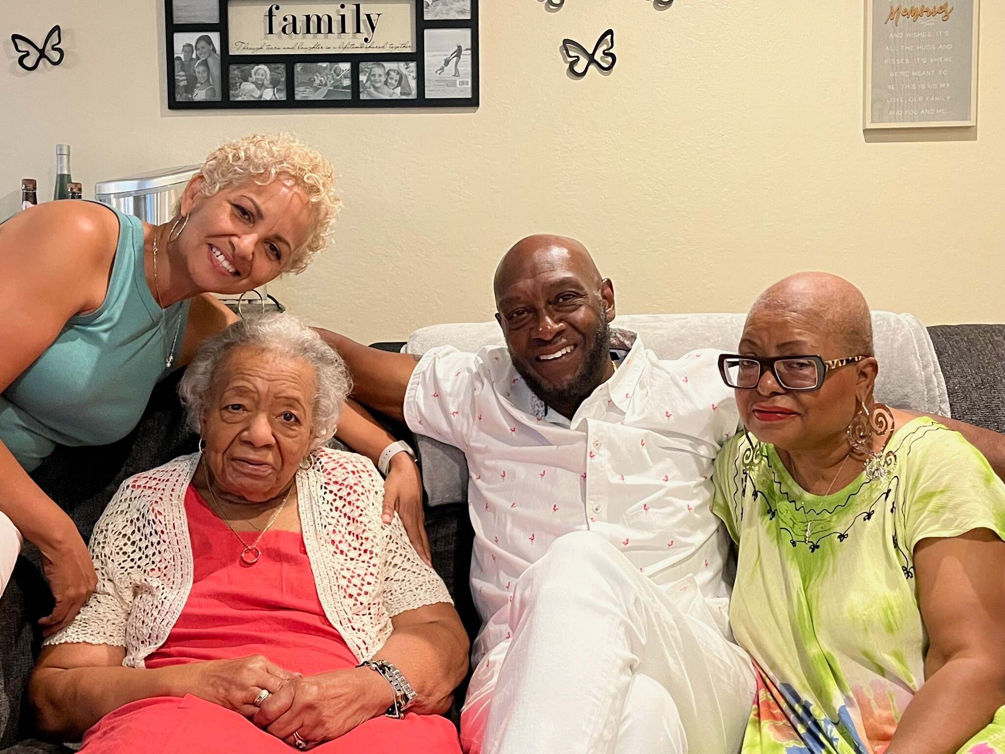 Four adults posed on a sofa, smiling at the camera in a living room with butterfly wall decor behind them.