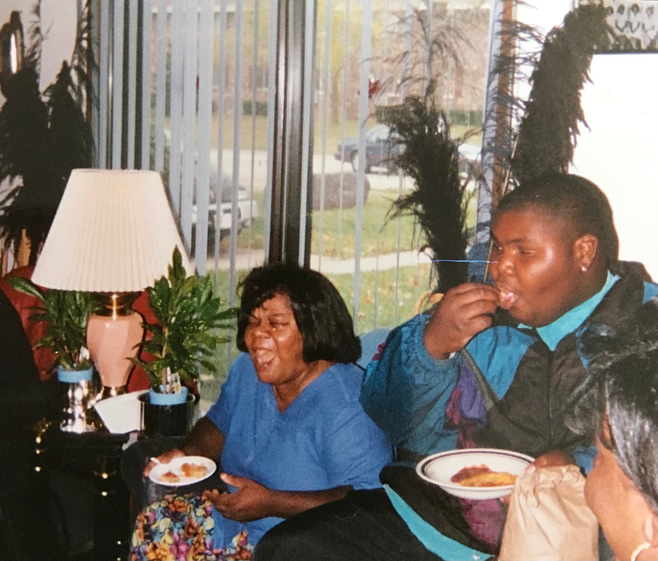 Smiling group dining indoors around a table with plates of food and a lamp in the background.