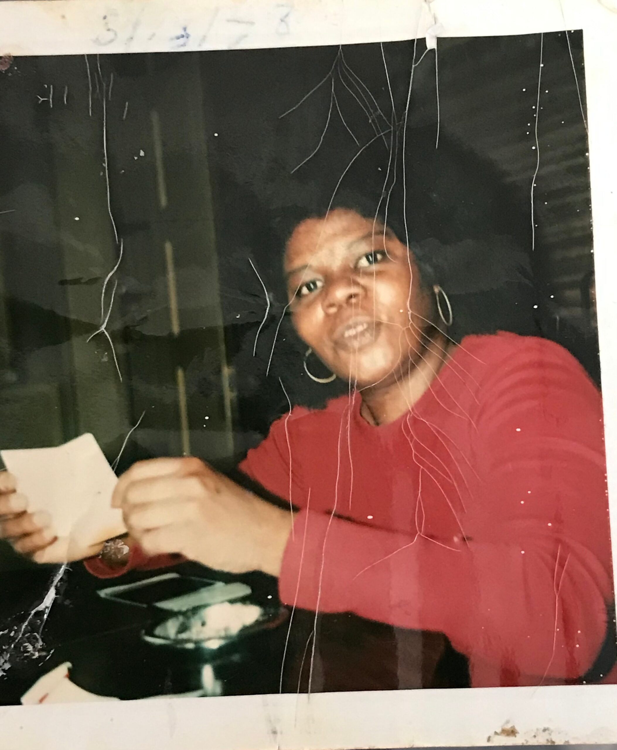 Person wearing a red shirt, looking at the camera, in a damaged photo with many scratches and marks.