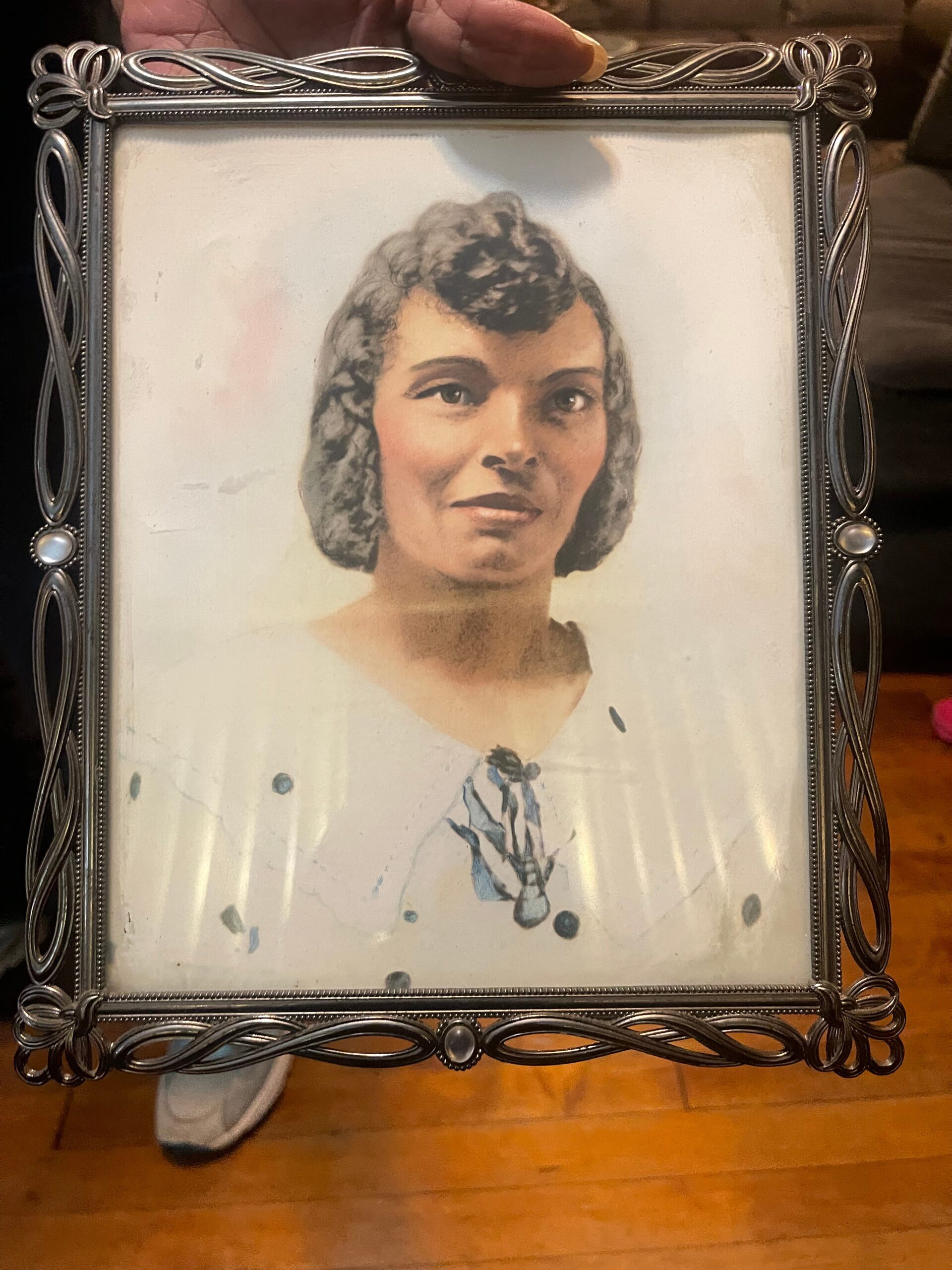Framed vintage portrait of a smiling woman with dark hair, inside an ornate silver frame held by a hand