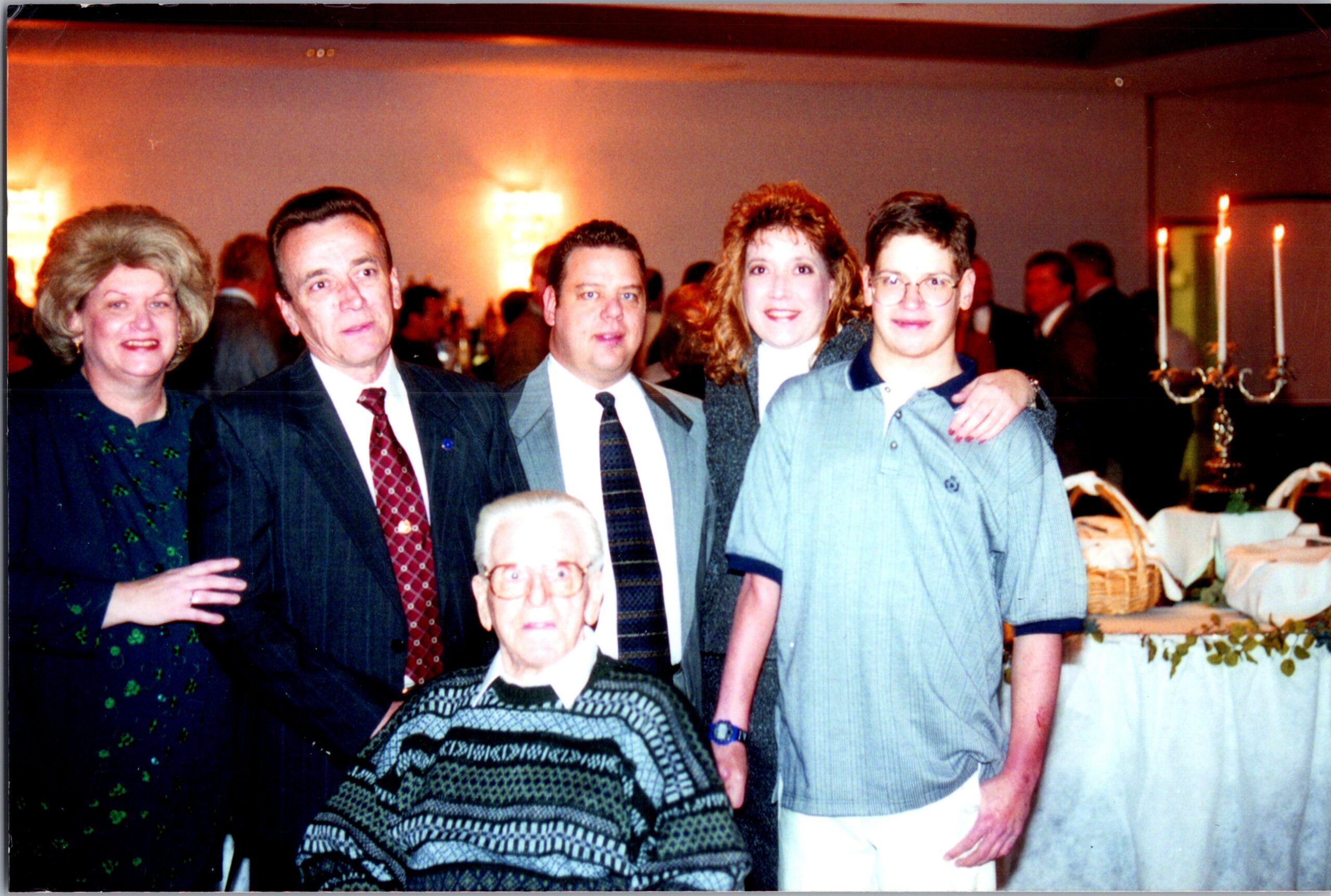 Six people pose for a group photo at a banquet, with candles and tables in the background.