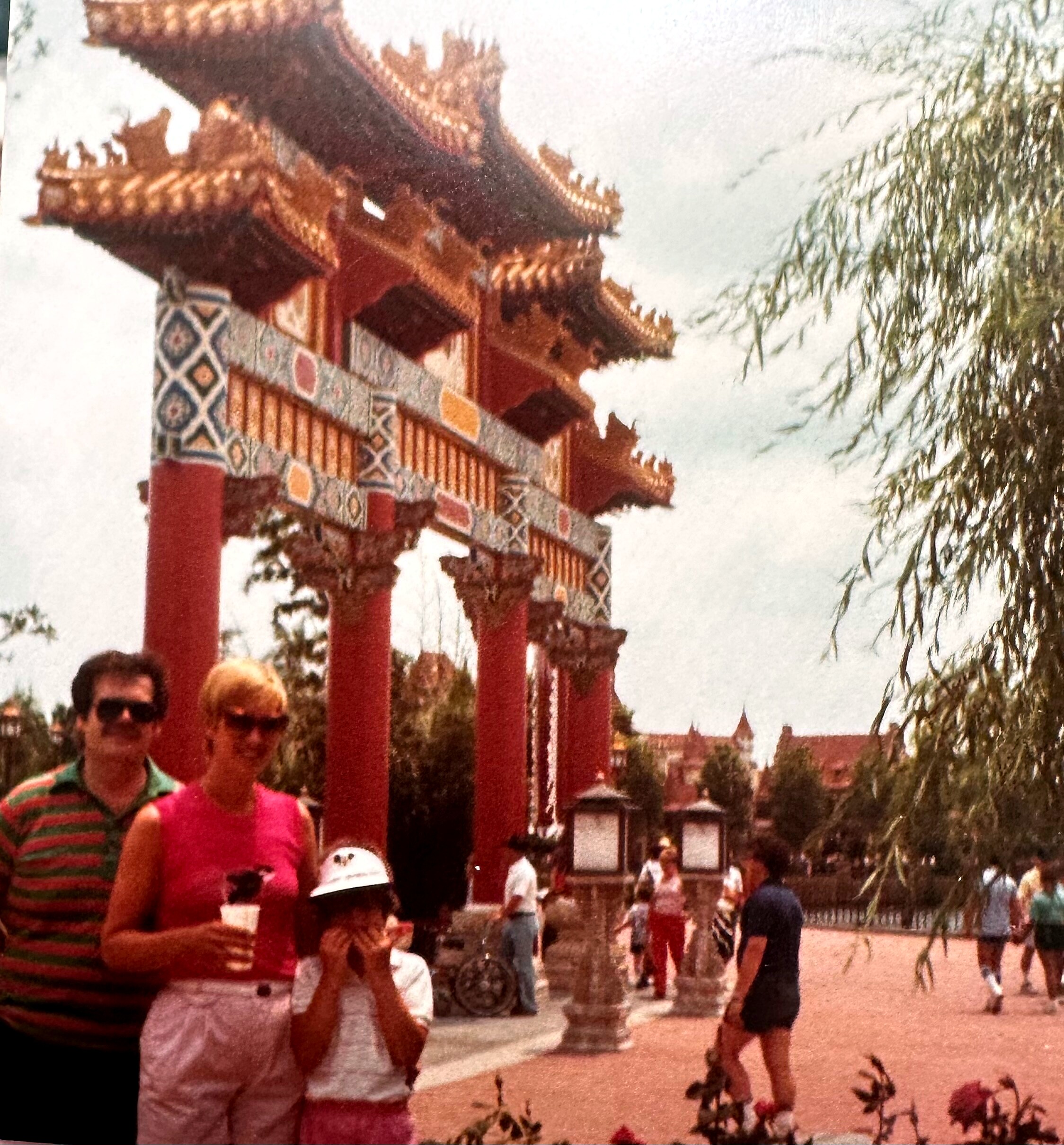 Group of people posing in front of a traditional Chinese pavilion with red columns and ornate roof, in a park setting.