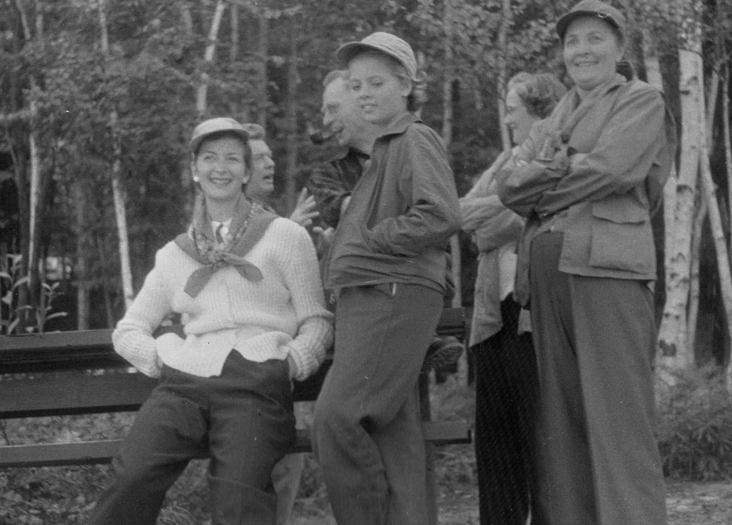 Group of four men and women posing outdoors, seated on a bench and standing behind it, smiling at the camera in a park setting.