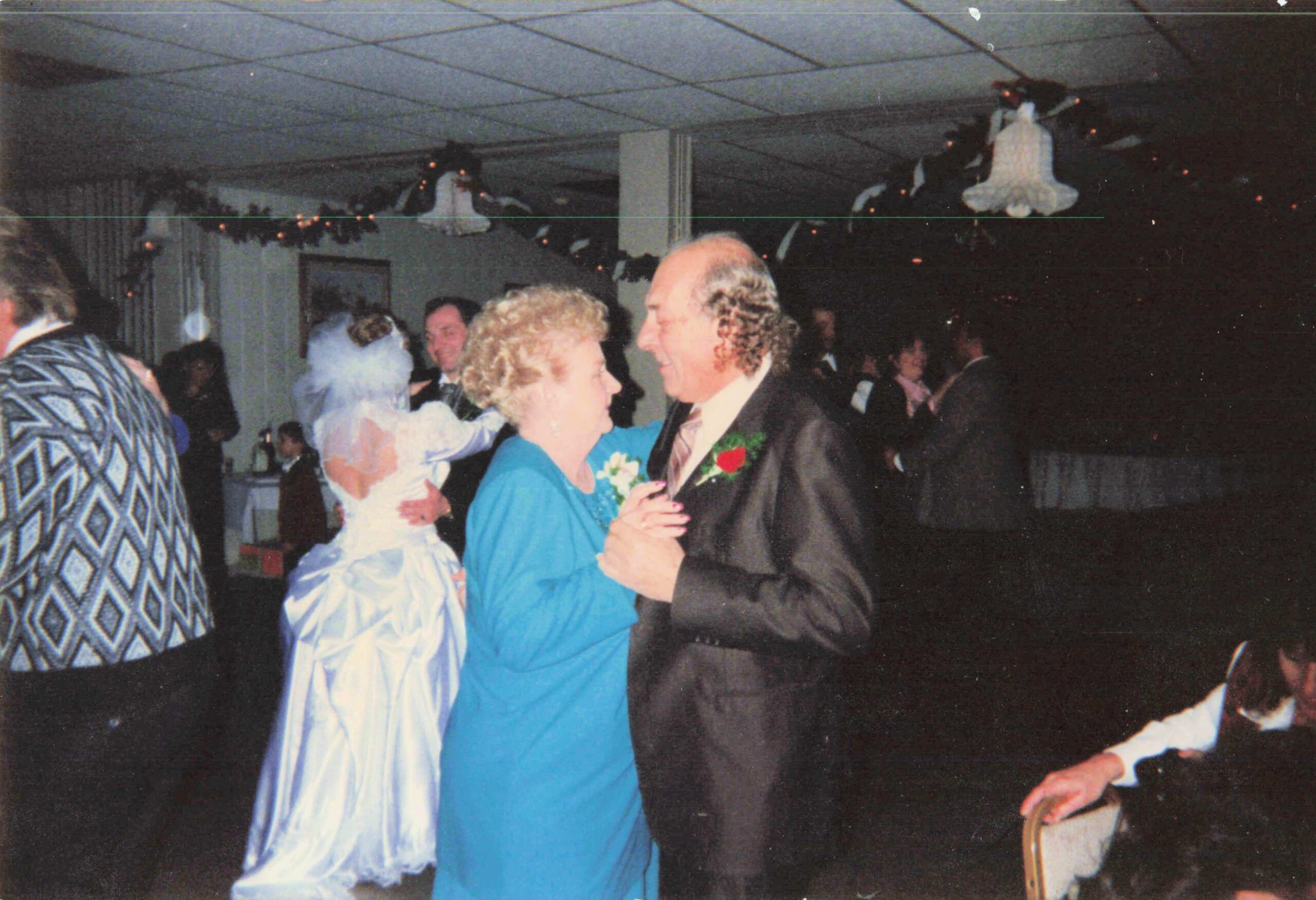 Couple dancing closely at a formal party, the man in a dark suit and the woman in a bright blue dress, with festive decorations in the background.