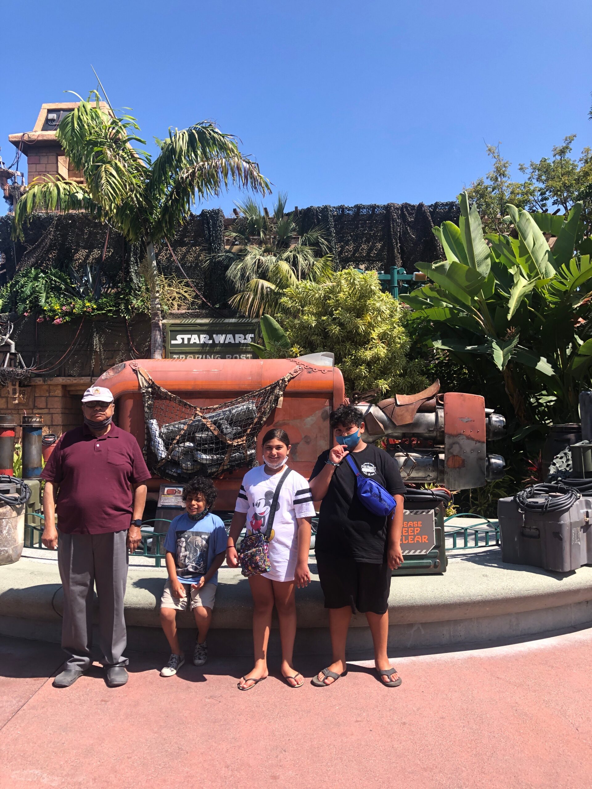 A family of five poses for a photo in front of a Star Wars display with an orange vehicle and tropical plants in the background.