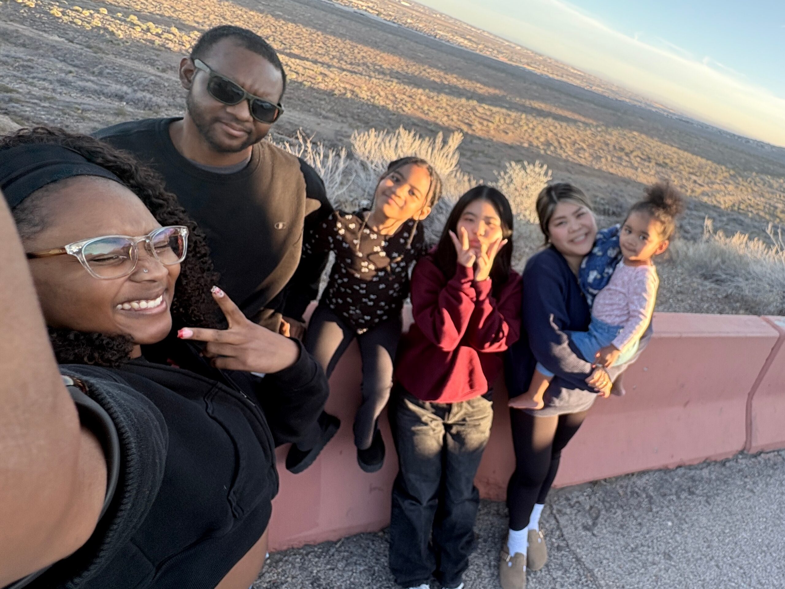 Group of friends taking a sunset selfie on a hillside, leaning on a pink barrier and smiling at the camera.