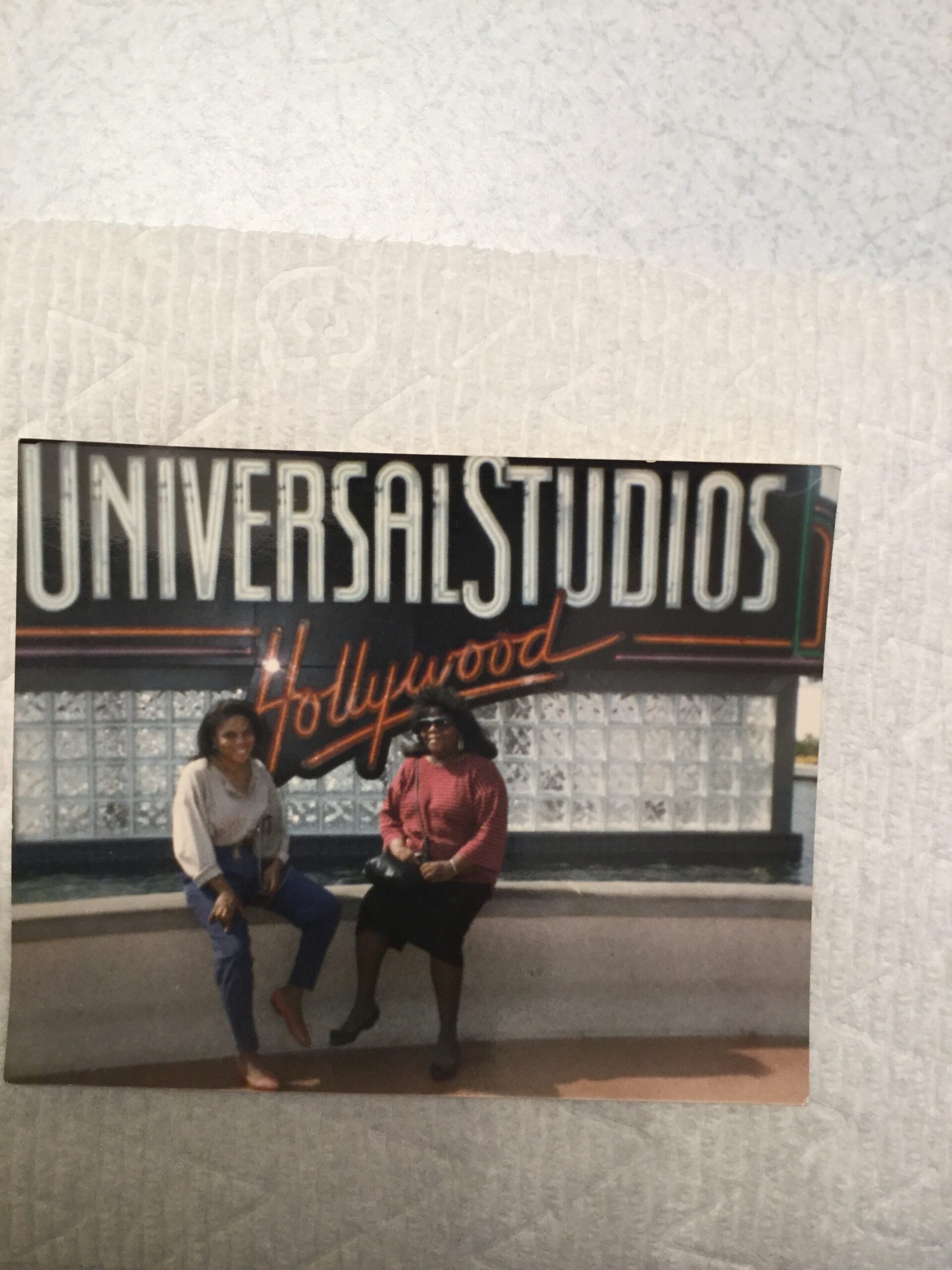Two people posing in front of a large Universal Studios Hollywood sign with neon “Hollywood” lettering in the background.