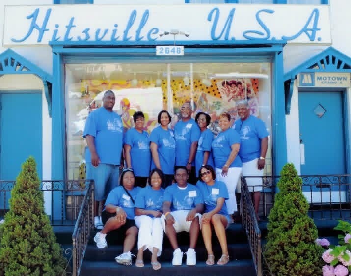 Group of twelve people in matching blue shirts posing on the front steps of the Hitsville U.S.A. storefront.