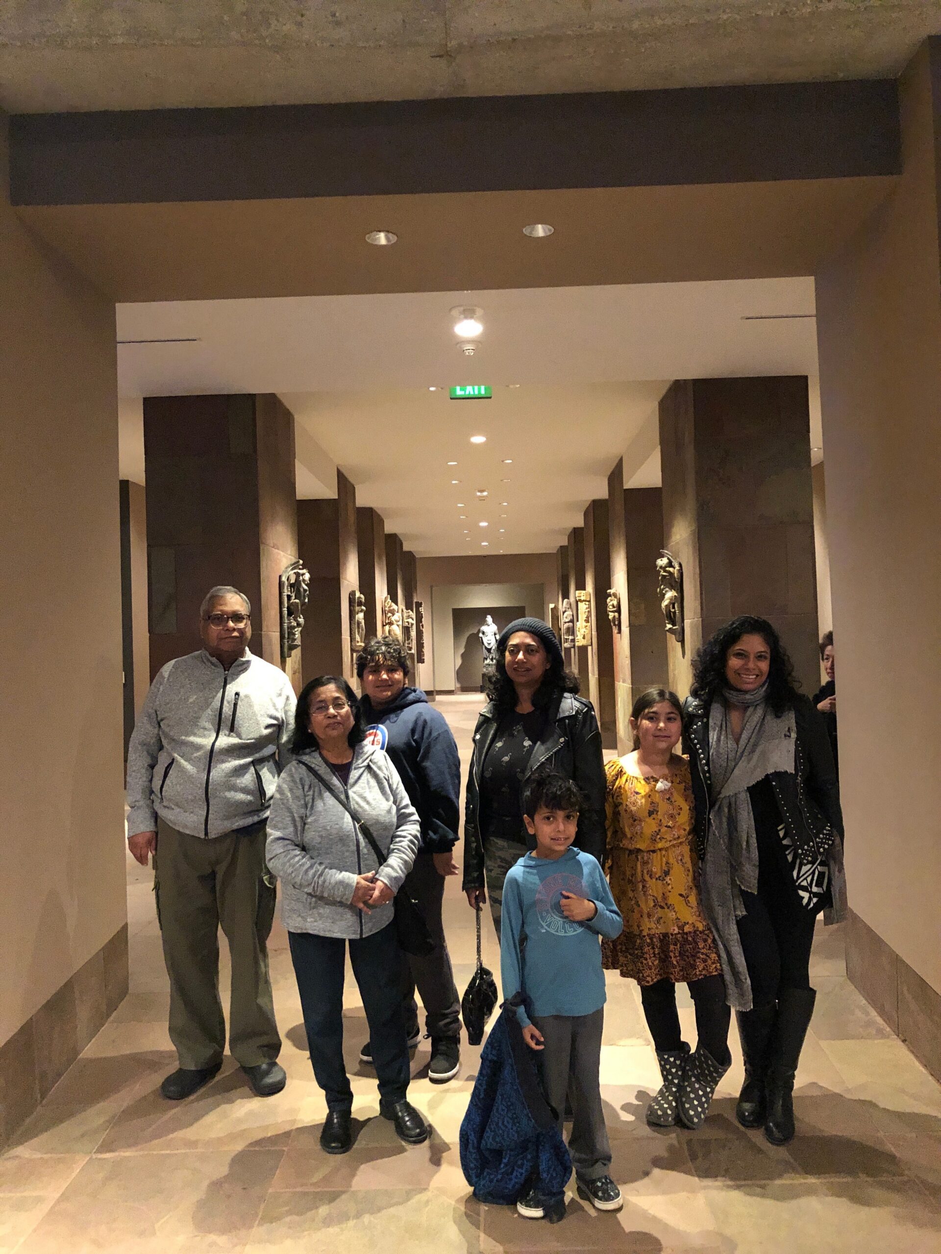 Group of people posing together in a museum hallway lined with display alcoves and sculptures behind them