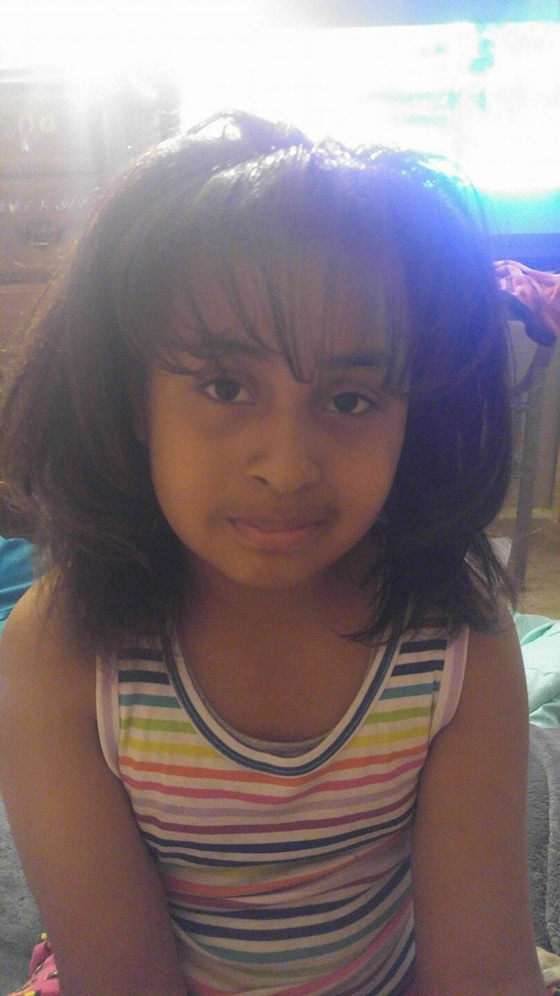 Young girl with shoulder-length dark hair wearing a rainbow-striped tank top, looking at the camera.