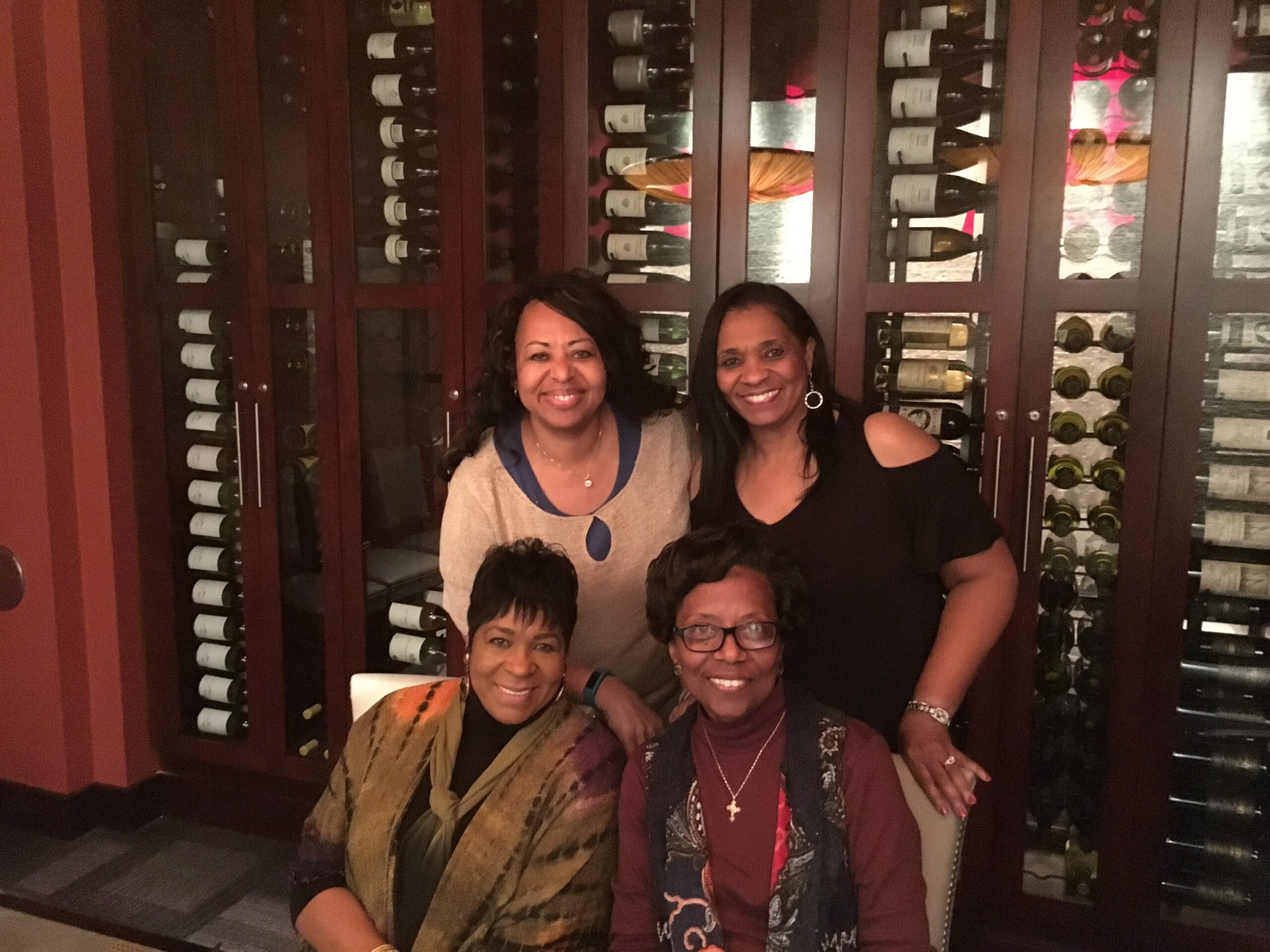 Five women posing together in a wine cellar with tall wooden racks of bottles behind them, smiling for the camera.