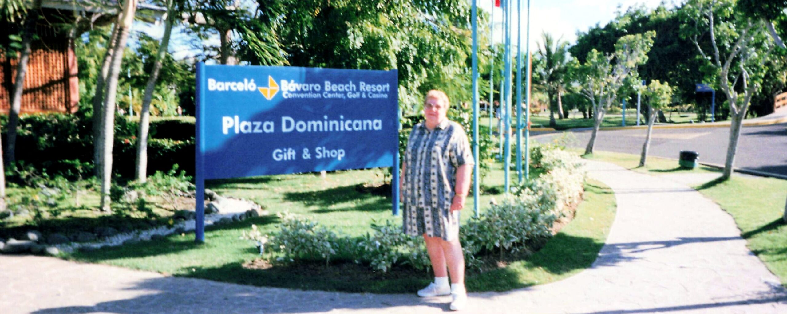 Woman standing beside a blue sign that says Plaza Dominicana Gift & Shop at Barcelo Bavaro Beach Resort.