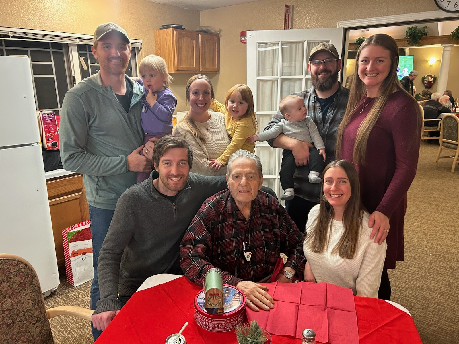 Multigenerational family gathered around a holiday table, smiling at the camera in a cozy room.
