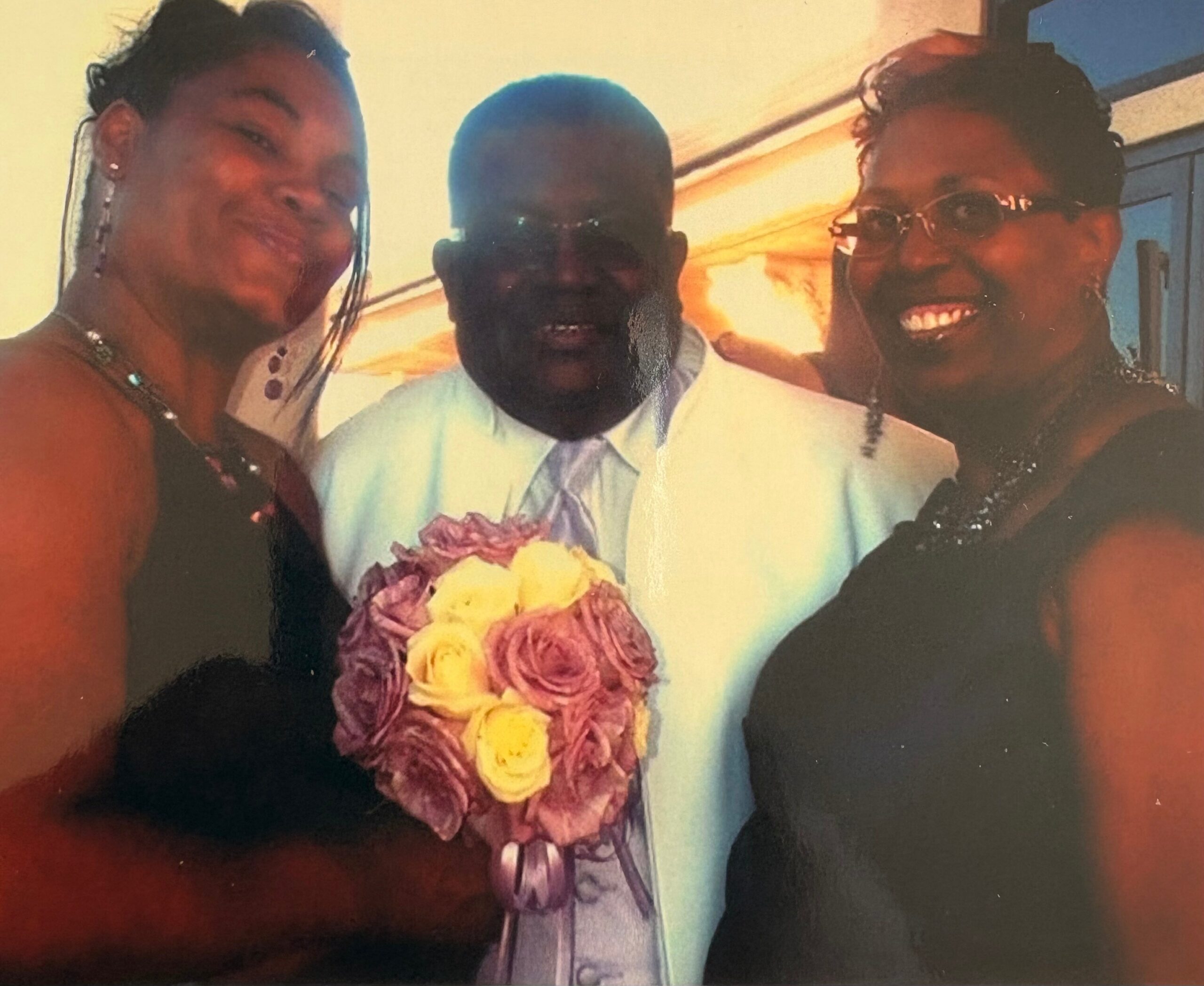 Three people smiling for a close-up group photo; center person wears a light shirt and a flower garland, flanked by two friends.
