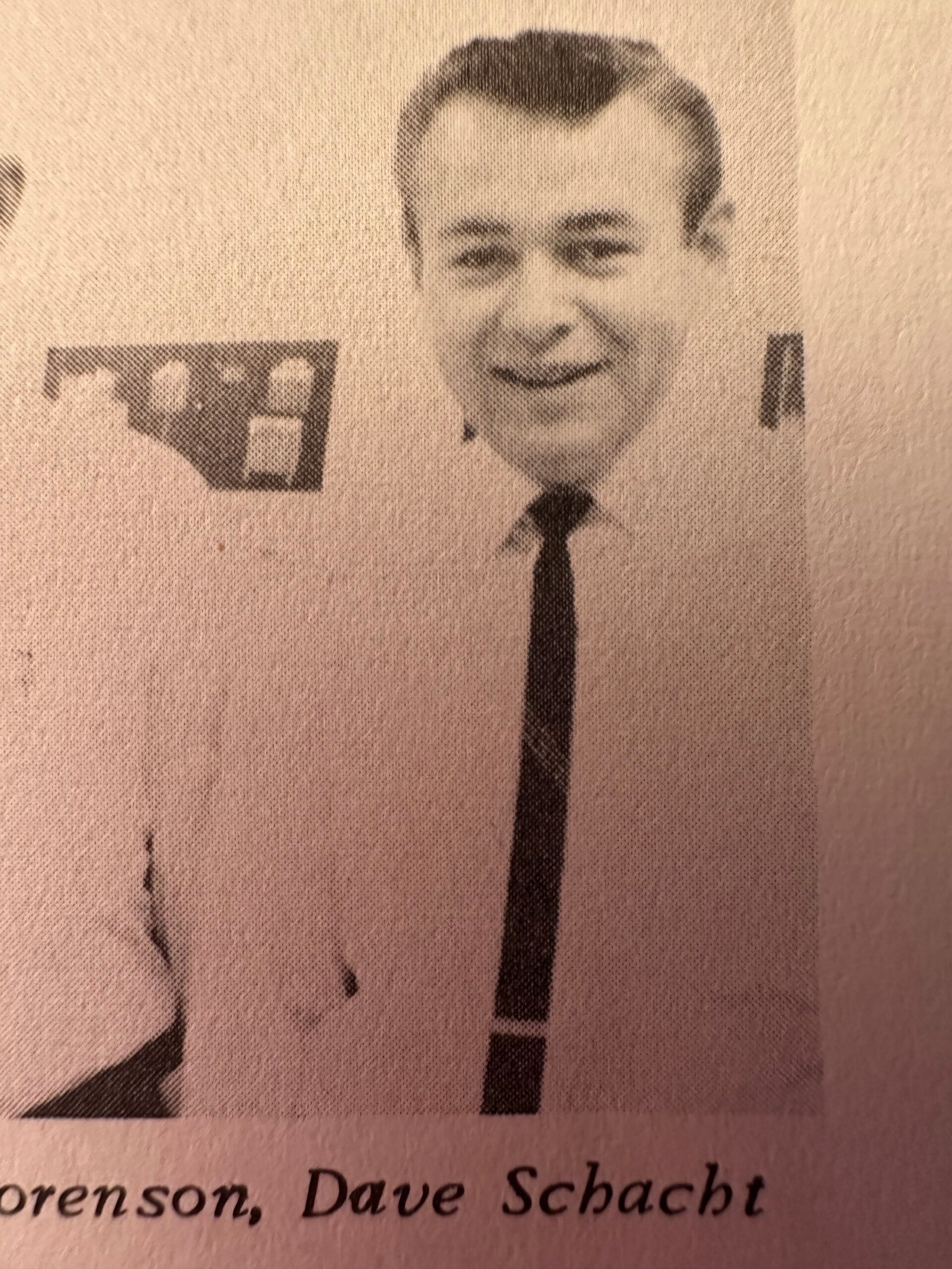 Black-and-white newspaper portrait of a smiling man in a suit and tie facing the camera.