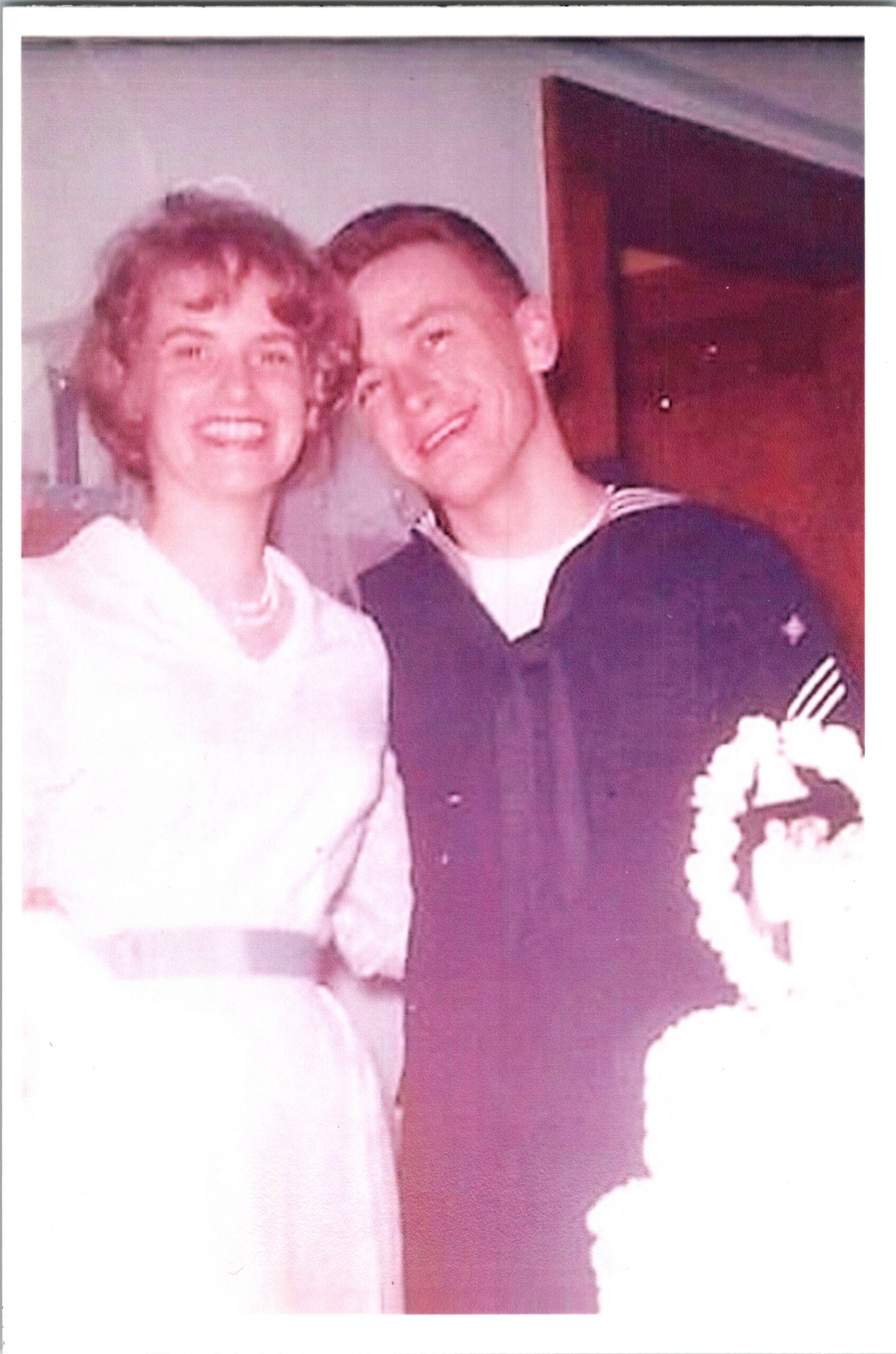 Smiling couple posing for a wedding photo: woman in a white dress and man in a dark suit.
