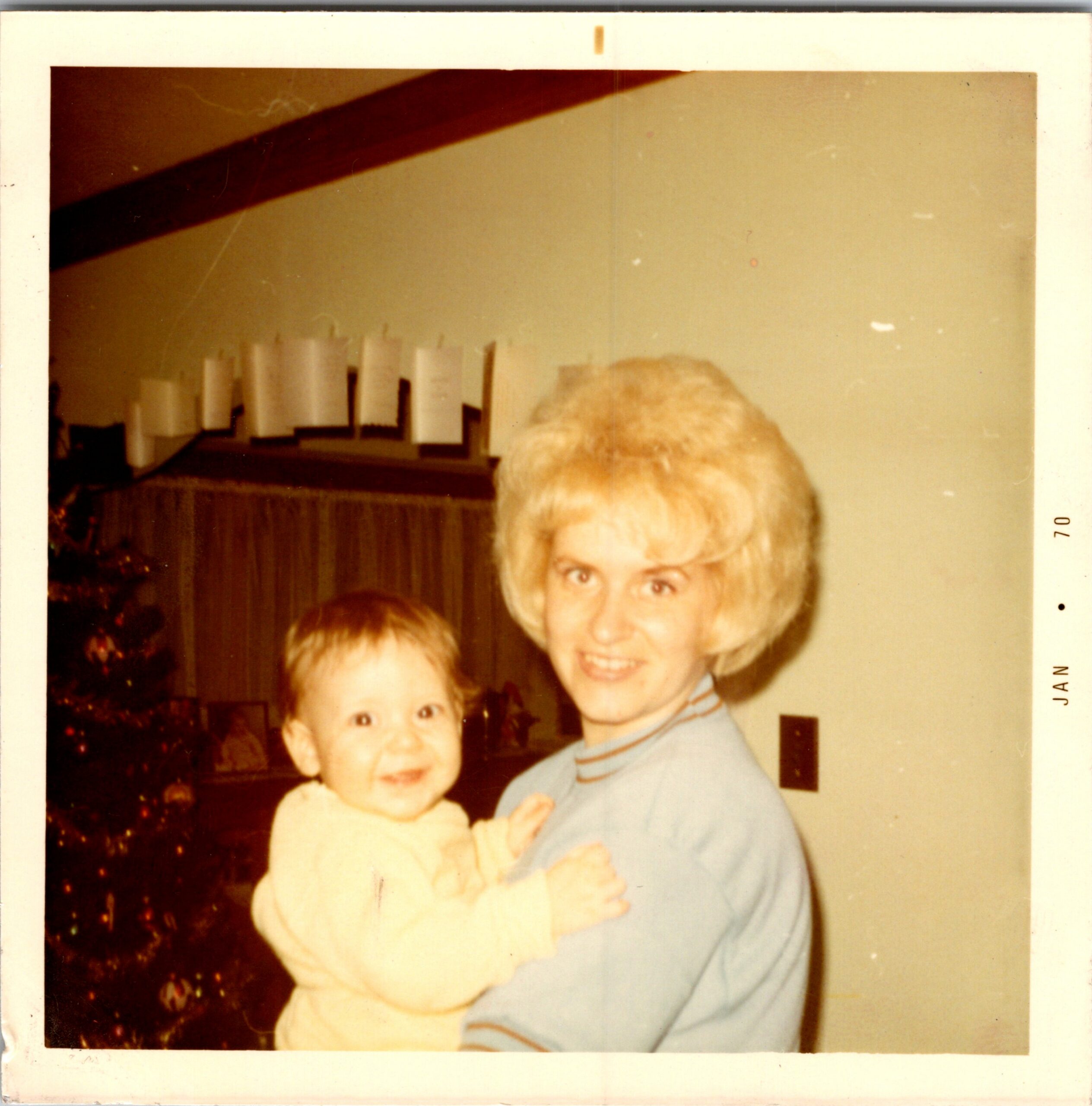 Polaroid-style family photo of a smiling woman with two young children indoors, a Christmas tree visible in the background behind them.