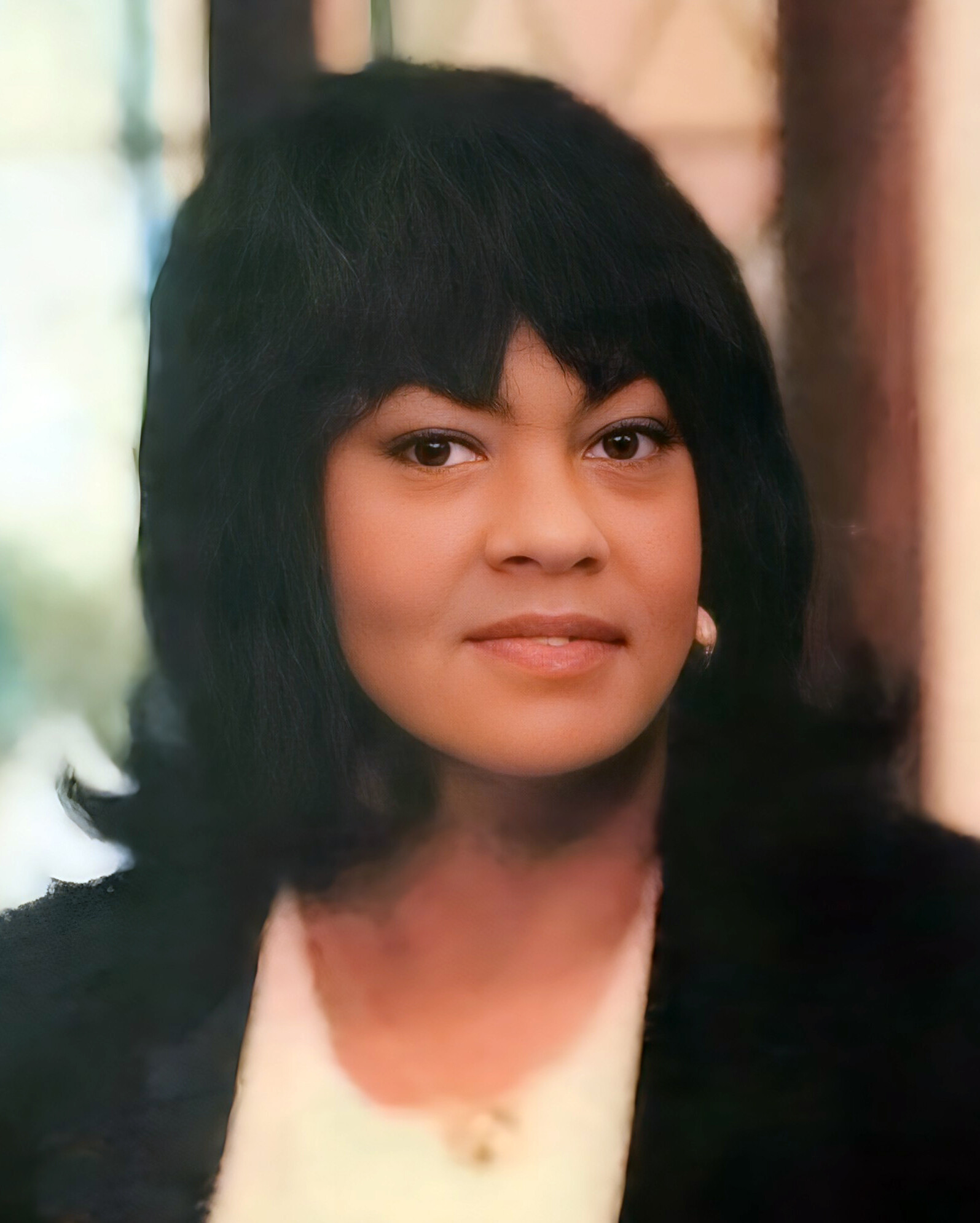 Close-up portrait of a woman with dark hair and warm skin, looking at the camera with a soft, blurred background.