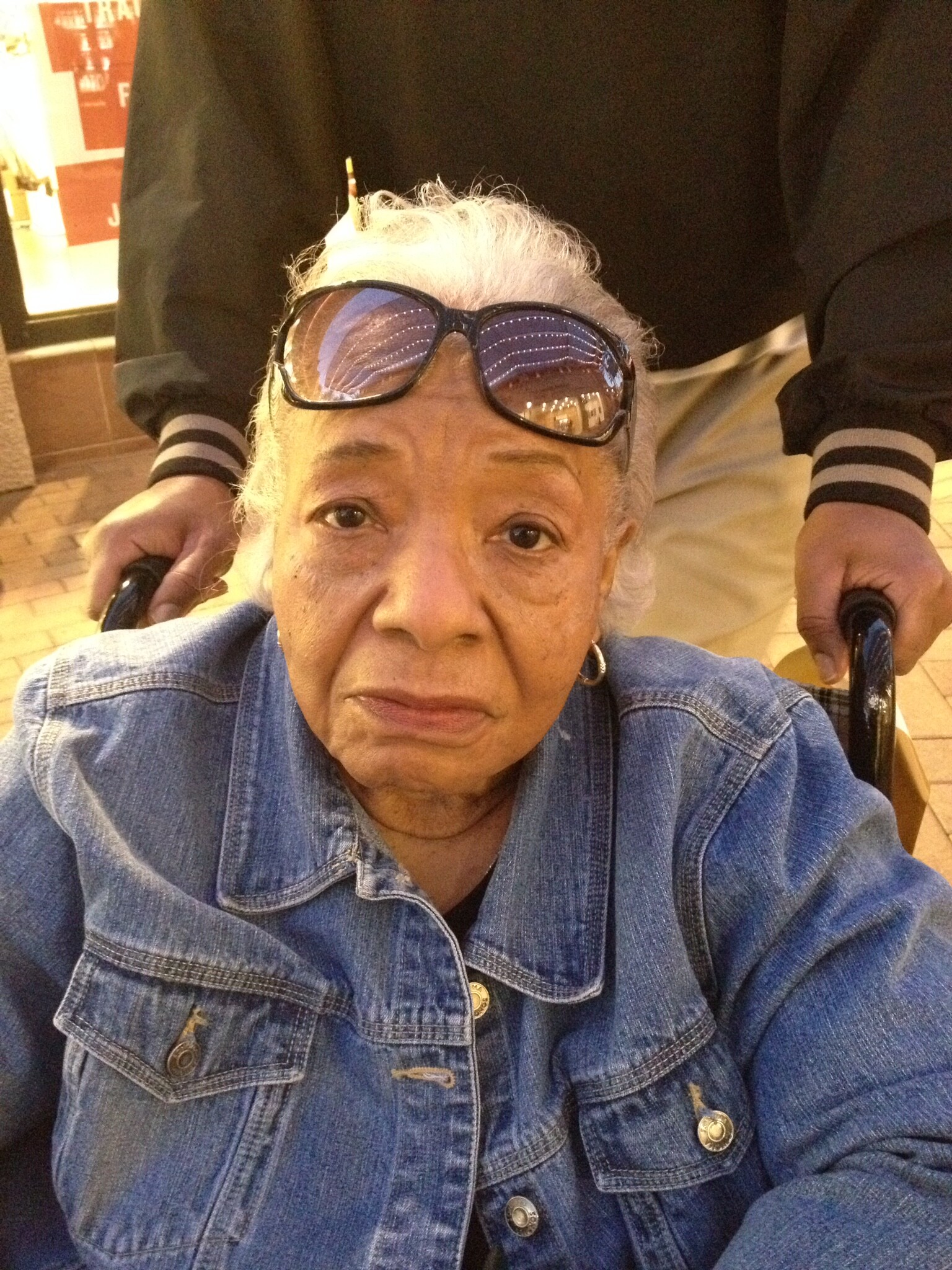 Close-up selfie of an elderly woman with white hair, wearing sunglasses on her head and a denim jacket.