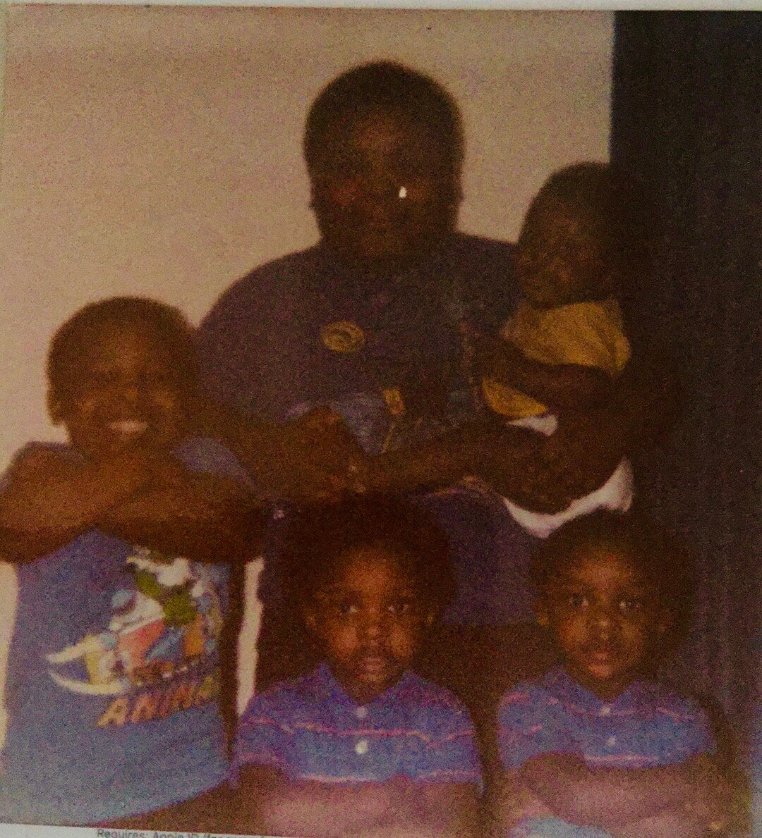 Family group portrait: father in purple shirt holding a baby, flanked by three children in blue outfits.