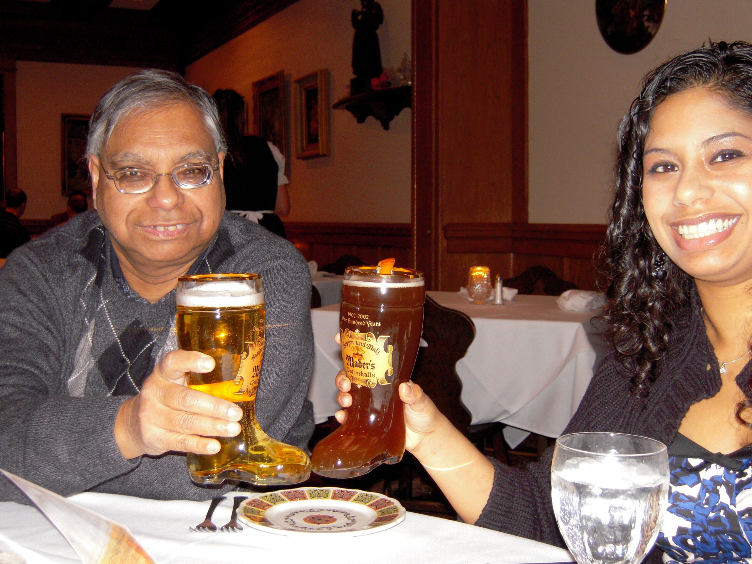Two friends toast with beer glasses at a restaurant, smiling at the camera.
