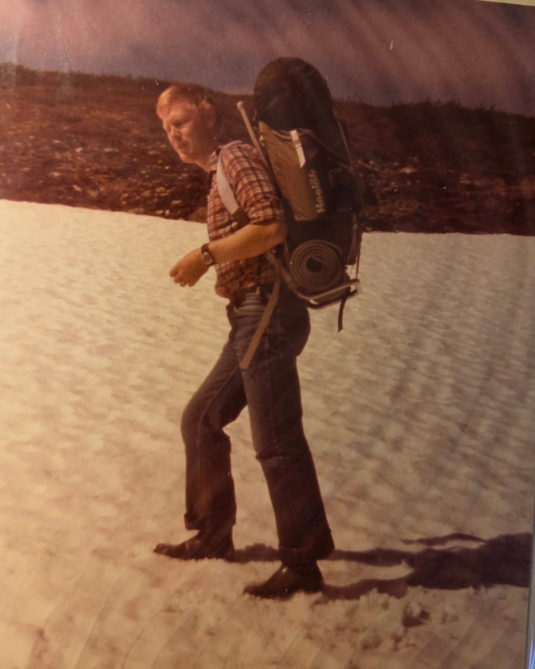 Hiker in a plaid shirt with a large backpack crossing a snowy landscape.