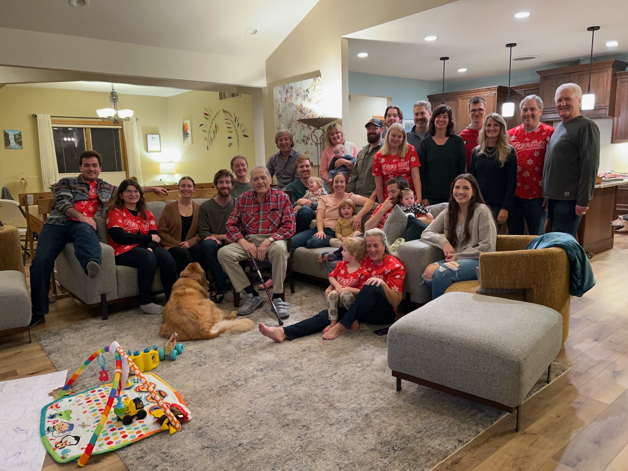 Large family gathering in a living room, people of various ages in red holiday shirts, smiling at the camera.