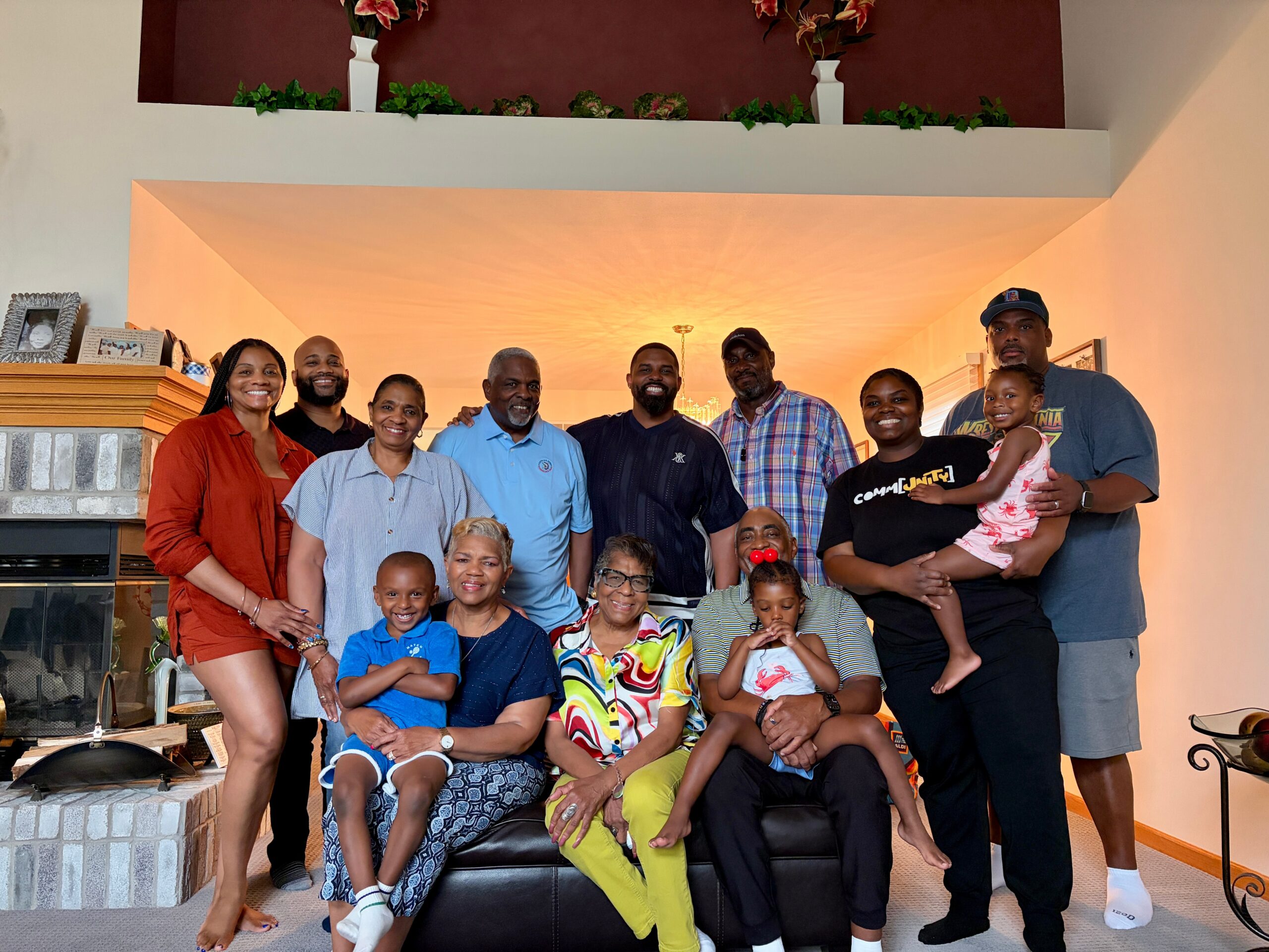 Large multiethnic group of adults and children posing together in a living room, smiling at the camera on a group photo.
