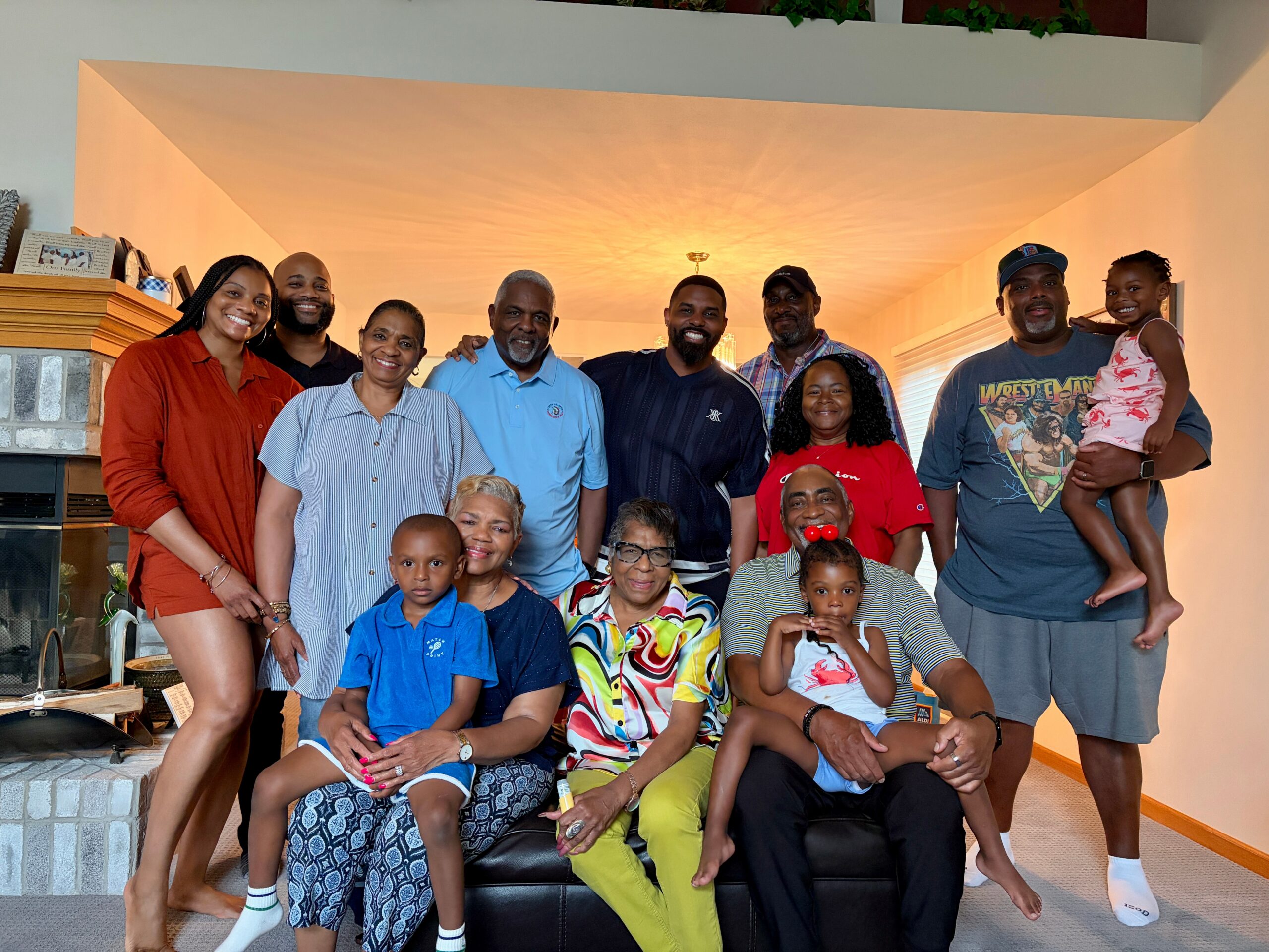 A large group of people smiling together in a living room for a family photo, with a fireplace on the left and warm lighting behind them.