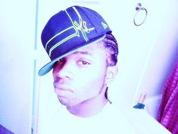 Portrait of a young man wearing a tilted baseball cap with lime-green stitching, looking at the camera in a bright room.