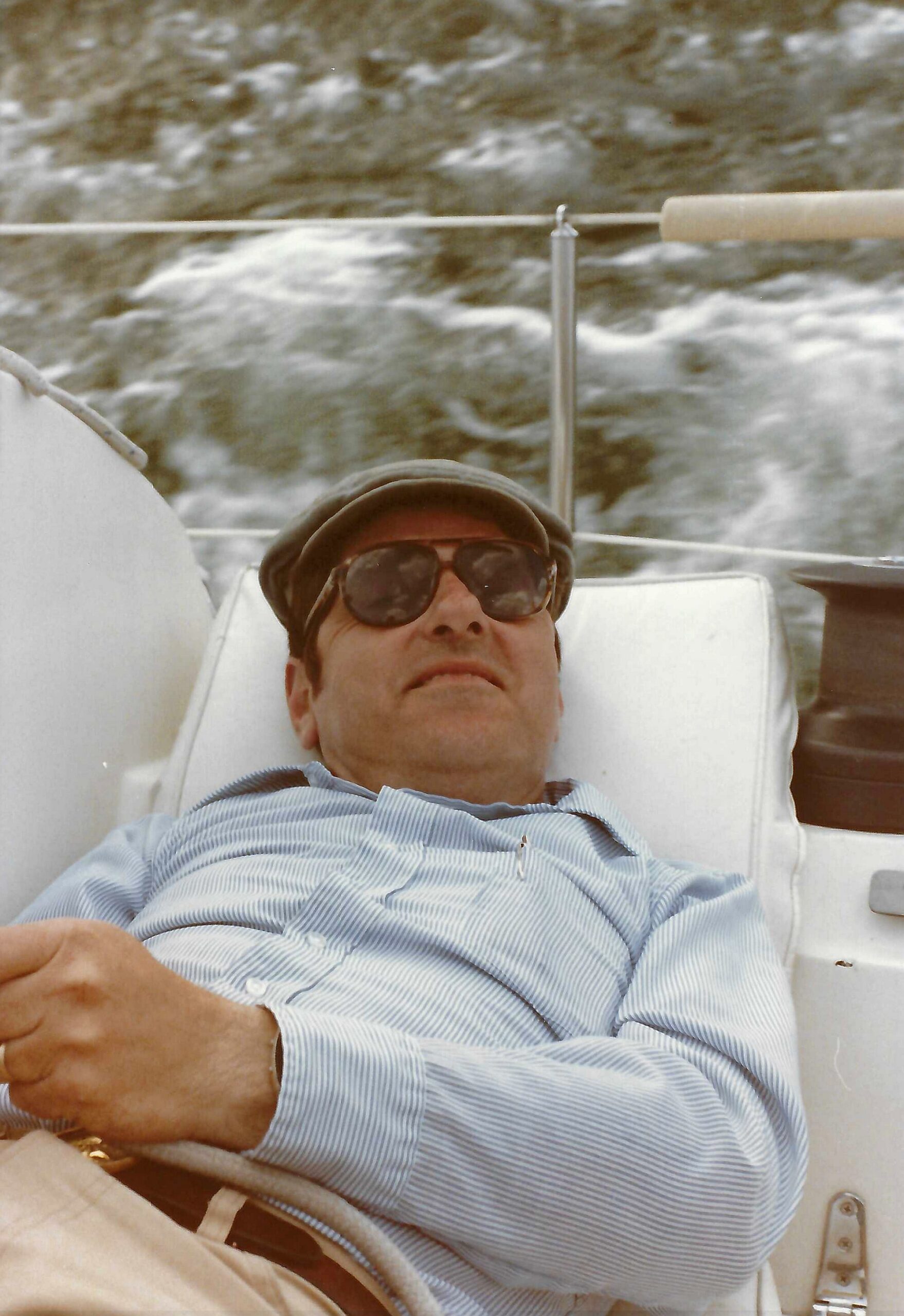 Man wearing a hat and sunglasses, reclining in a chair with snowy hills in the background.