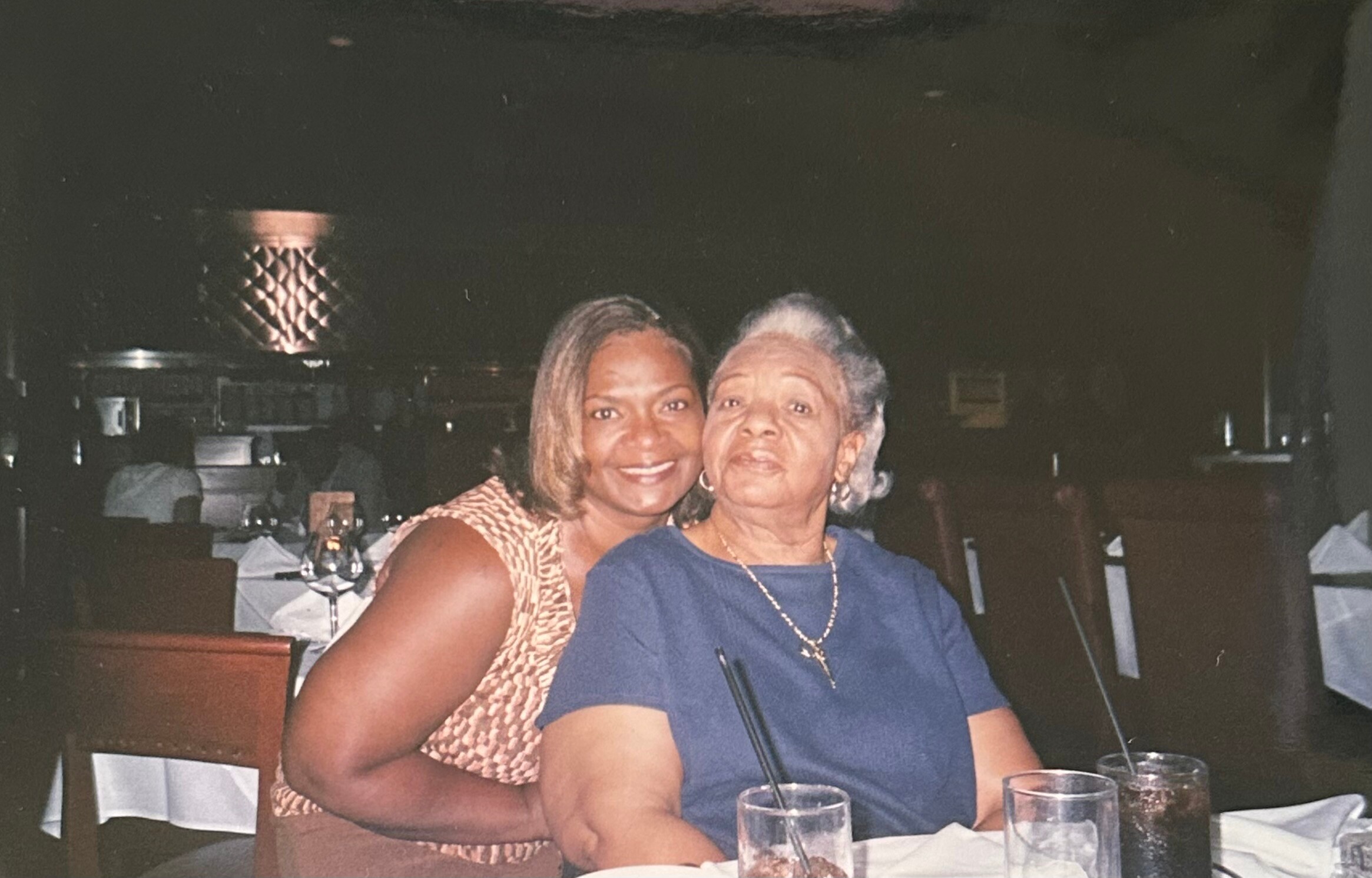Two women seated at a restaurant table, smiling for a photo at night-time dining setting.