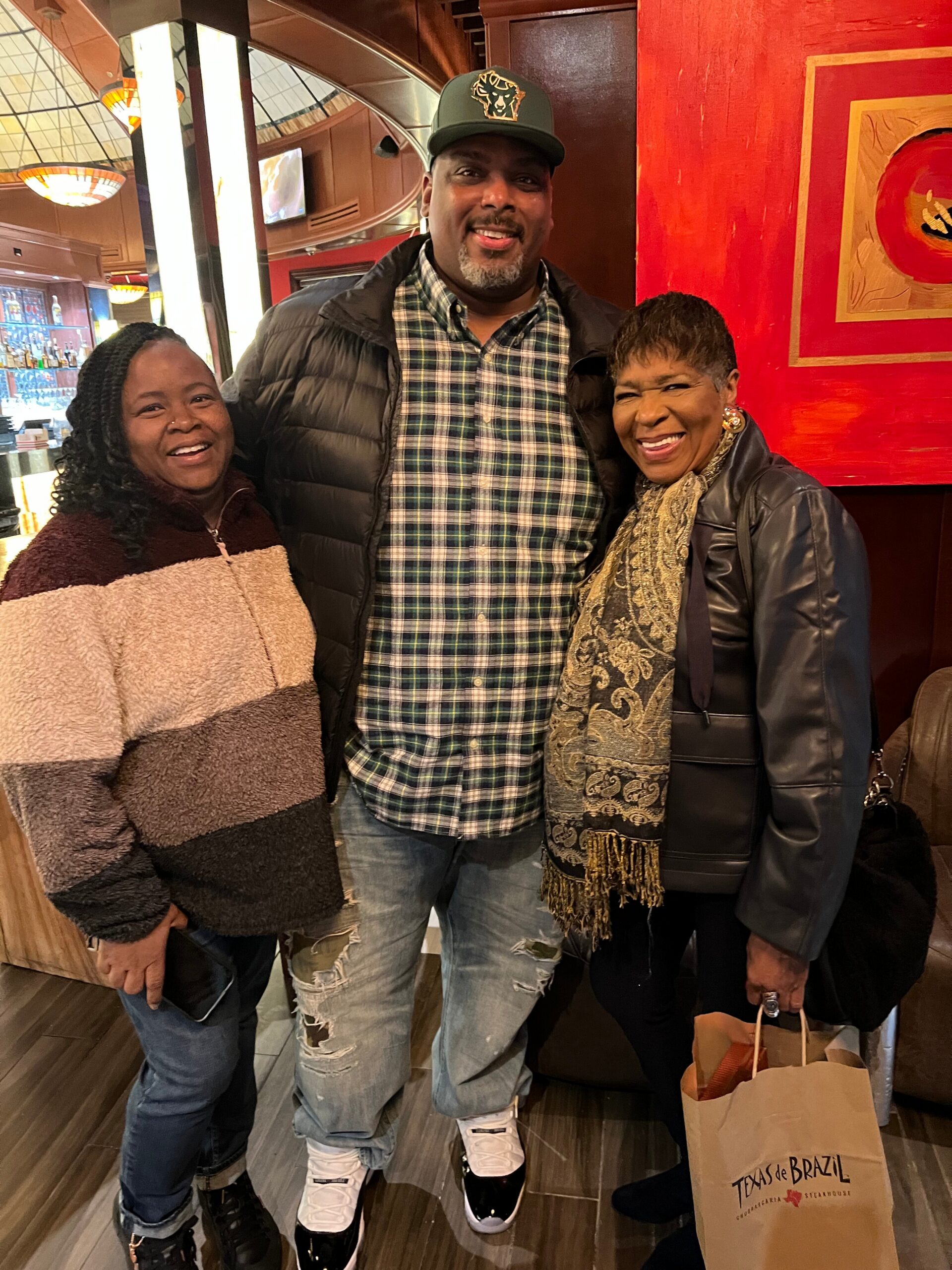 Three friends posing together inside a Texas de Brazil restaurant, smiling at the camera.