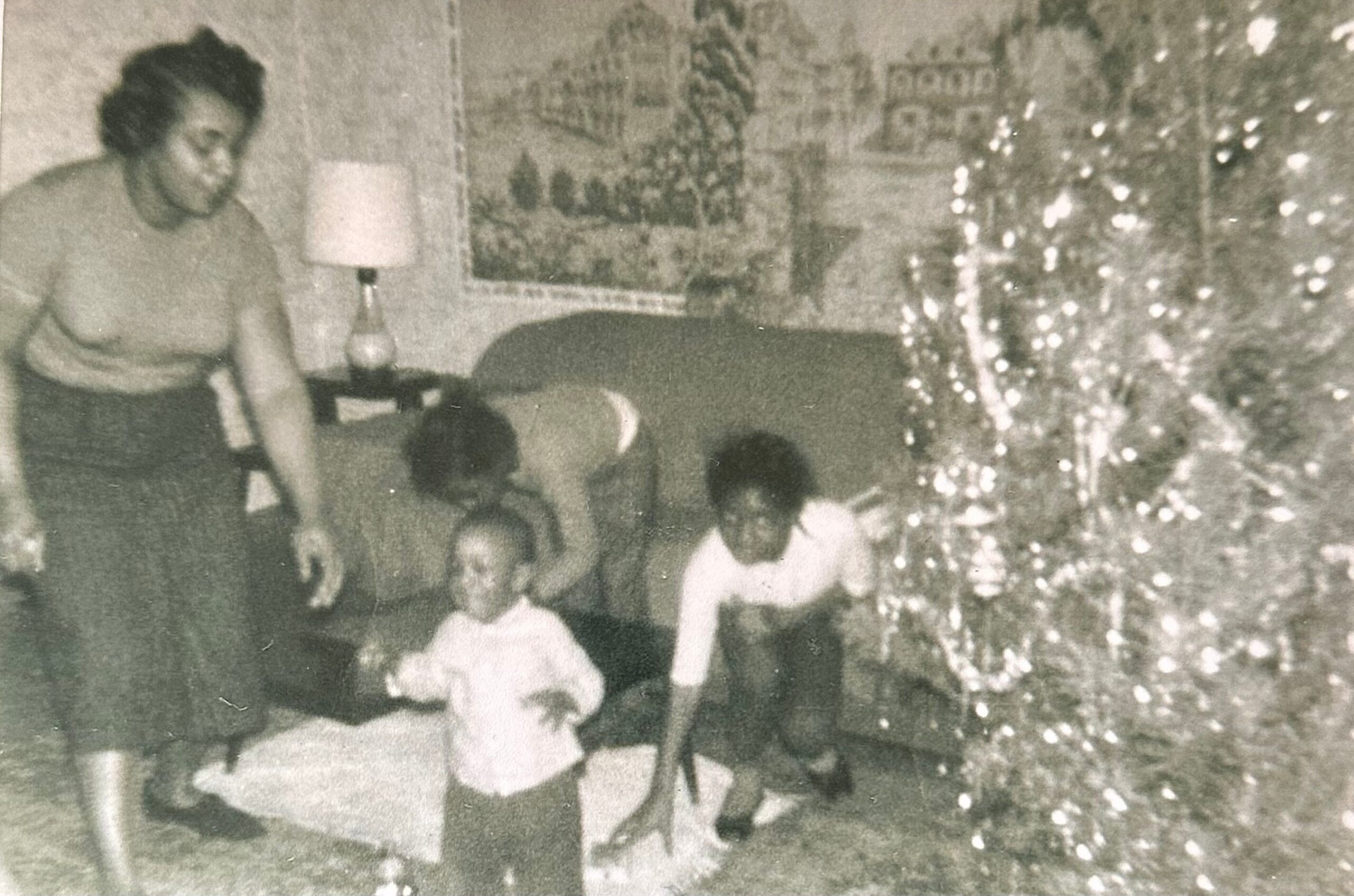 A family gathers in a living room around a lit Christmas tree, with adults and children smiling for a photo.