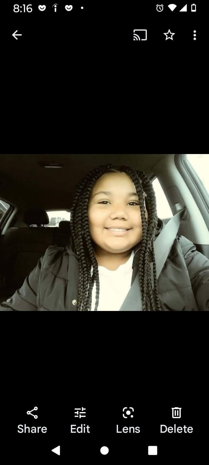 Young girl with braided hair smiling in a car, wearing a seat belt in the driver's seat.