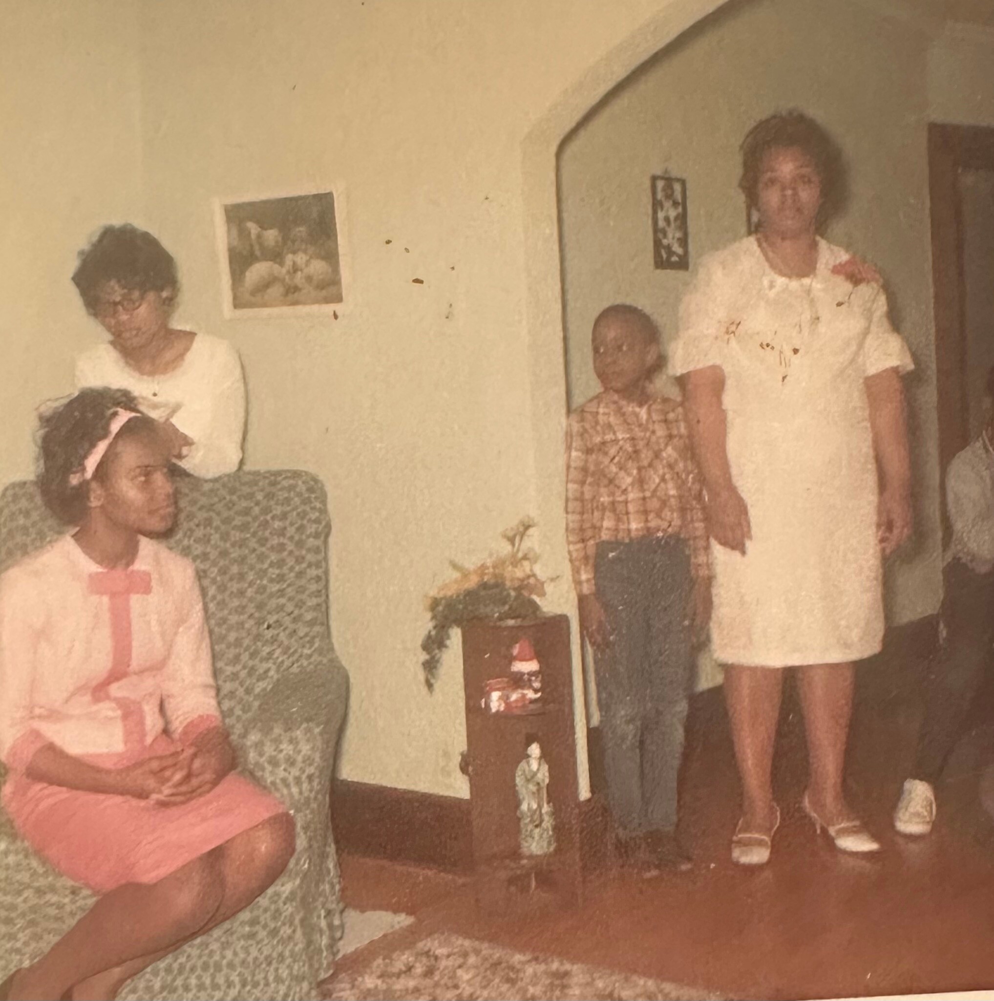 Family portrait from the 1960s: several adults pose indoors, wearing period clothing with soft colors and prints.
