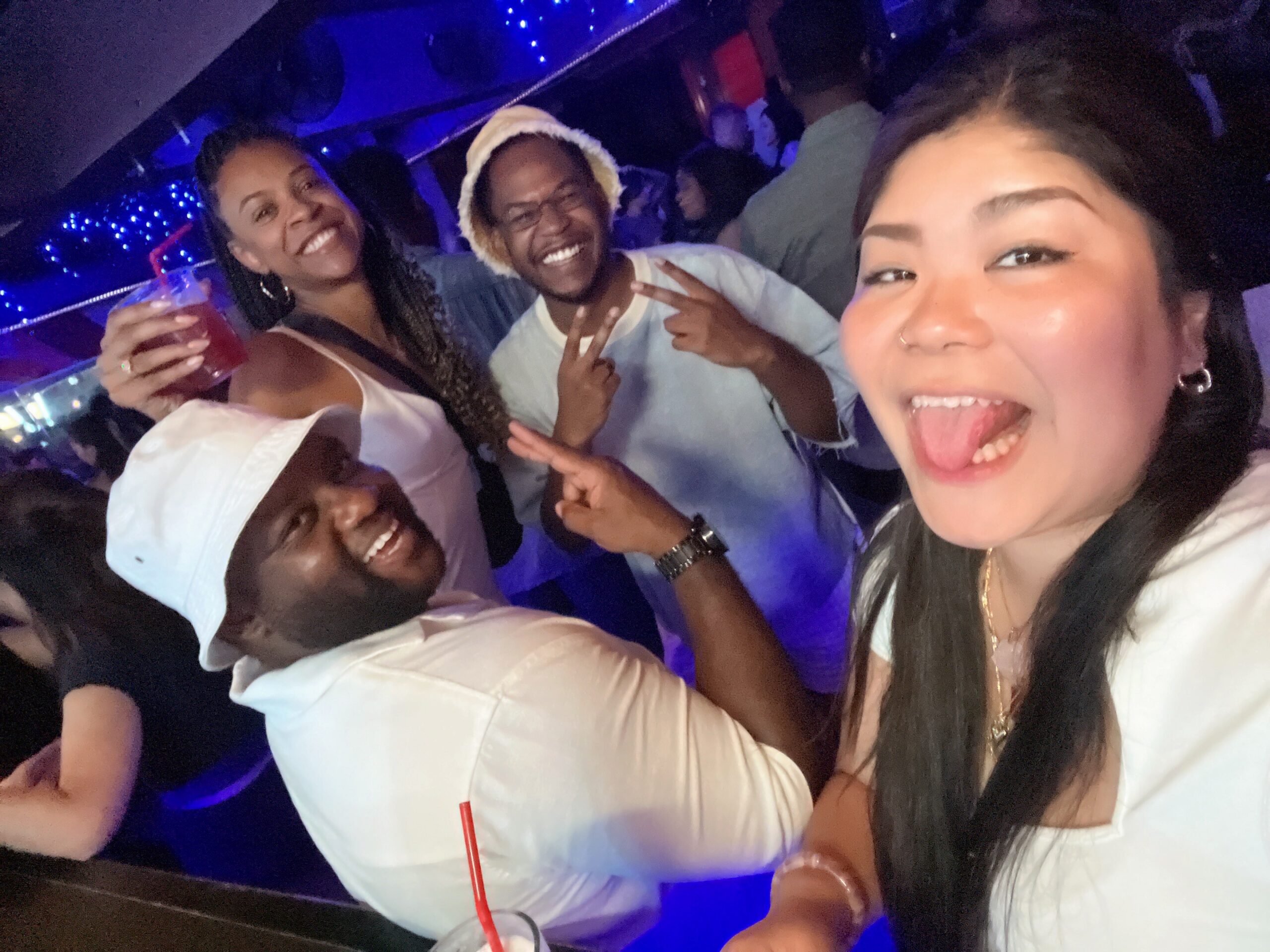 Group of friends taking a selfie at a crowded nighttime party, smiling and posing for the camera under blue lights.