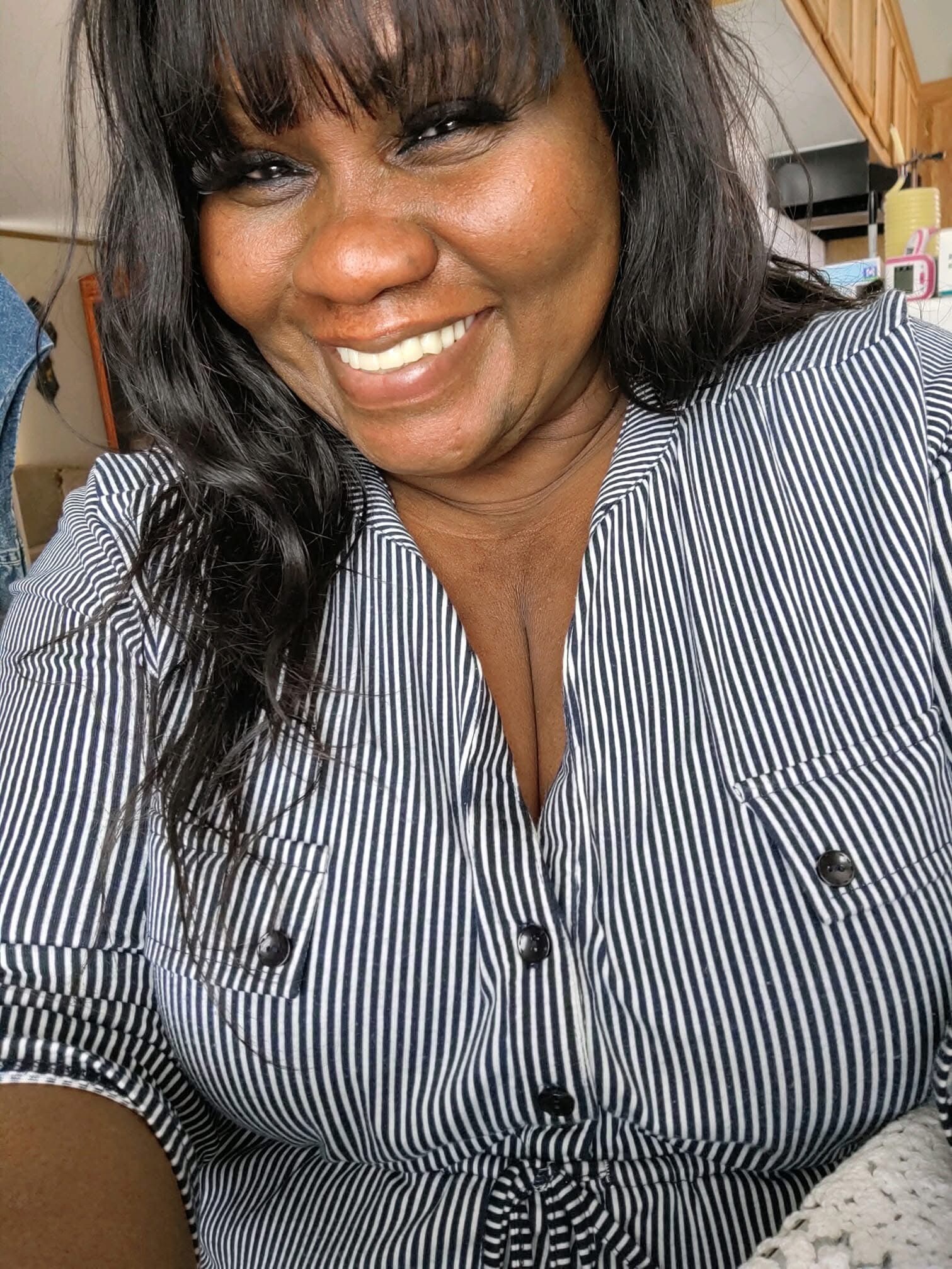 Close-up of a smiling woman with long dark hair wearing a navy-and-white striped button-up shirt.