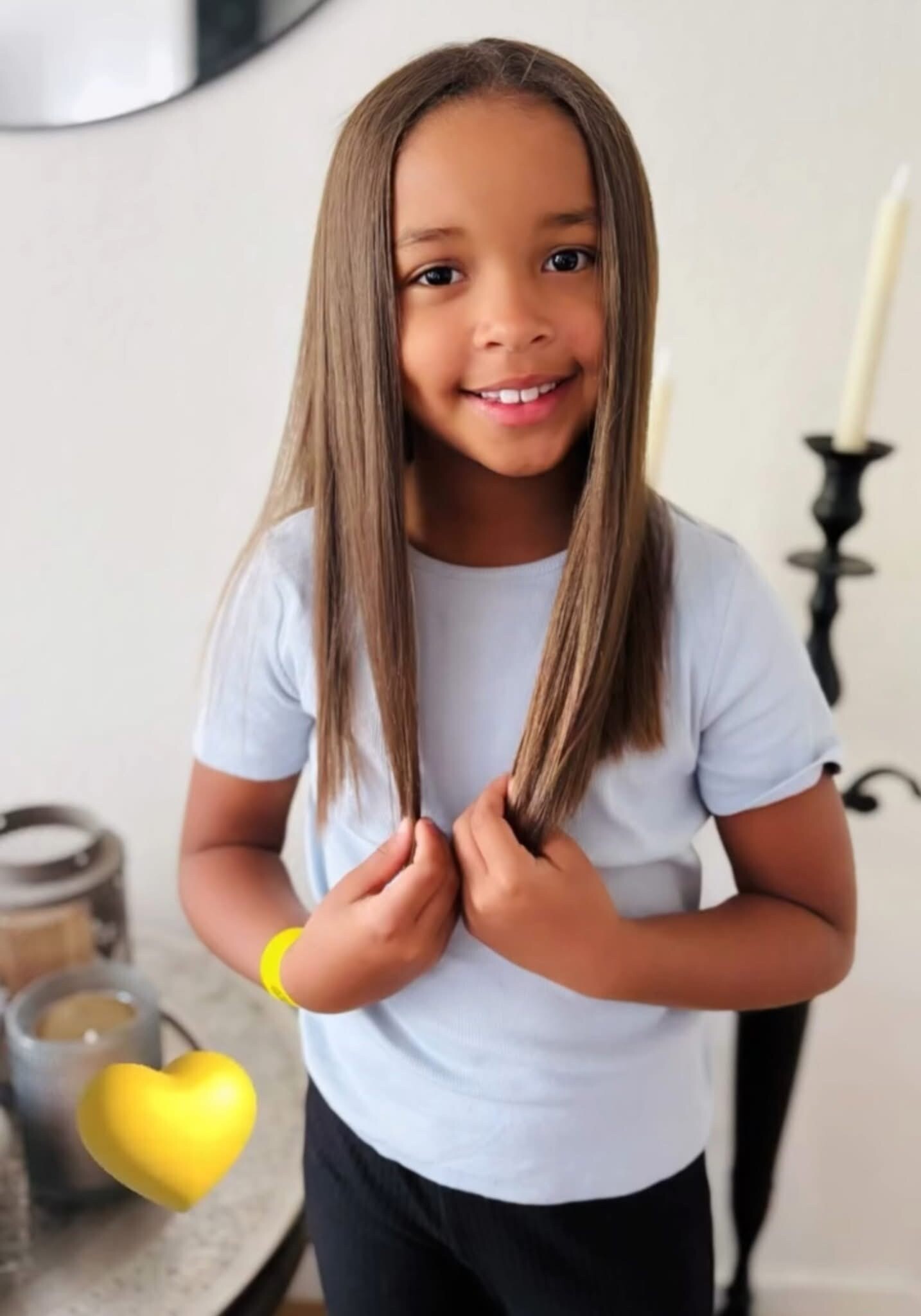 Smiling girl with long brown hair in a light blue shirt, standing in a kitchen near a lemon on the counter.