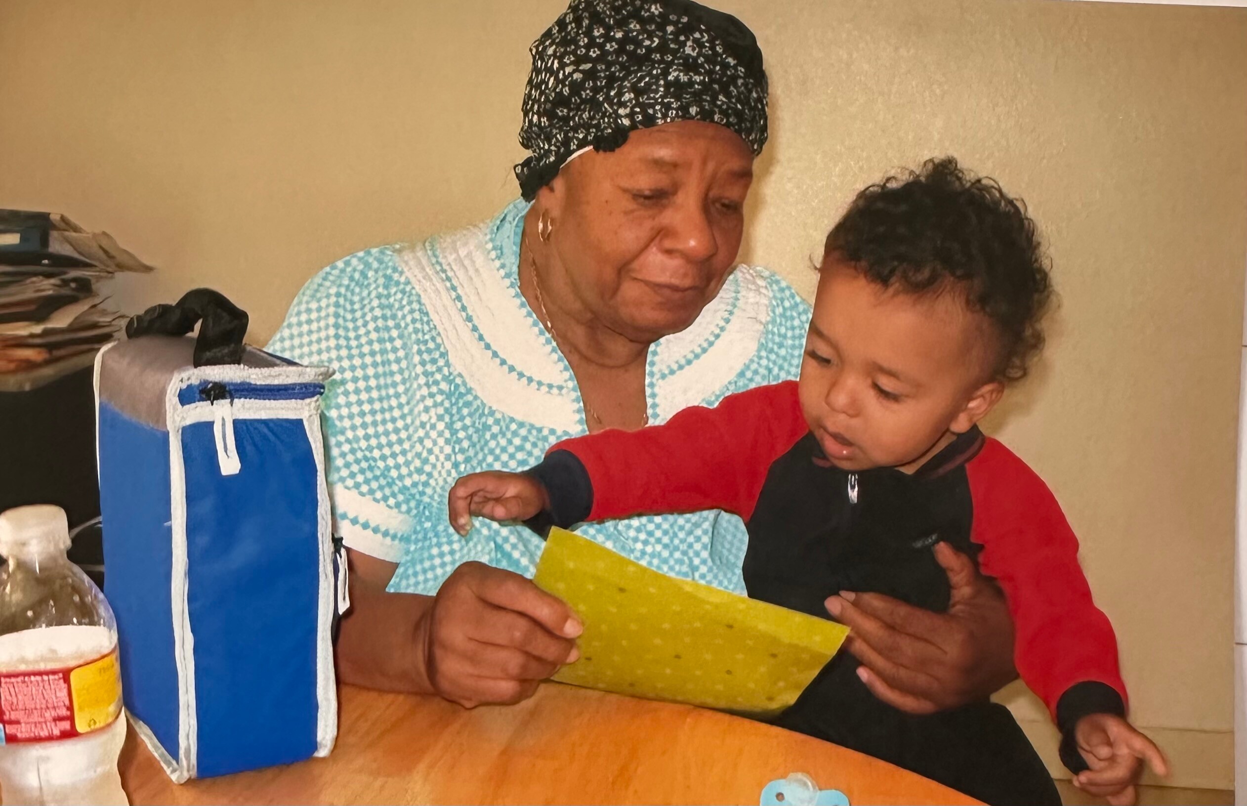 Grandmother and child looking at a yellow card together at a kitchen table with a blue lunch bag nearby