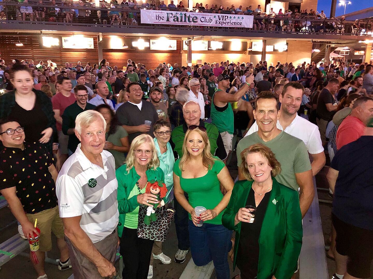 Group photo of a large, smiling crowd at a stadium-style venue, with a banner reading 'the Failte Club Experience' overhead.