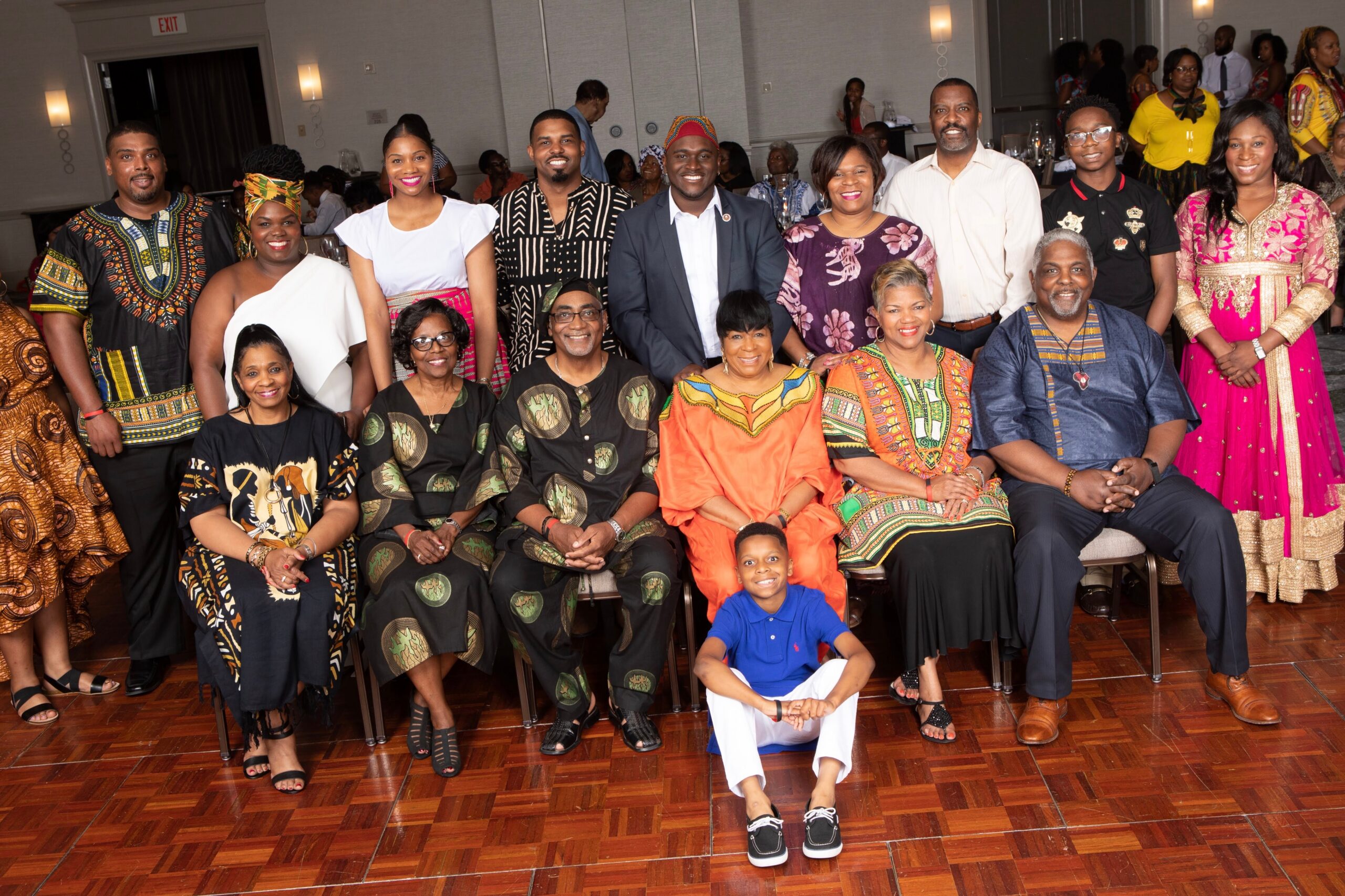 Large group of friends and family posing for a celebration photo in colorful traditional African attire at a banquet hall.