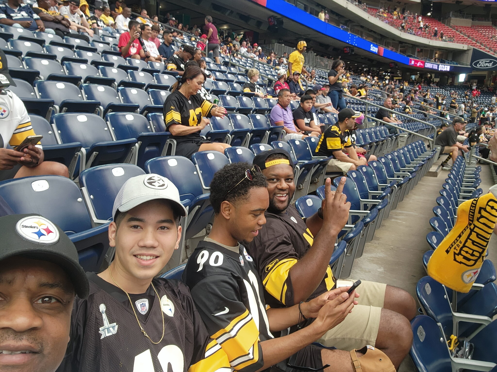 Group of Pittsburgh Steelers fans in black and gold jerseys seated in a stadium, taking selfies and chatting.