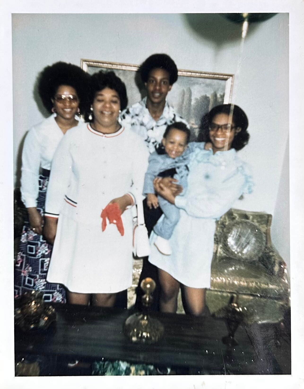 A family poses together in a living room, smiling for the photo (two women on each side, a man in back, a woman holds a baby).