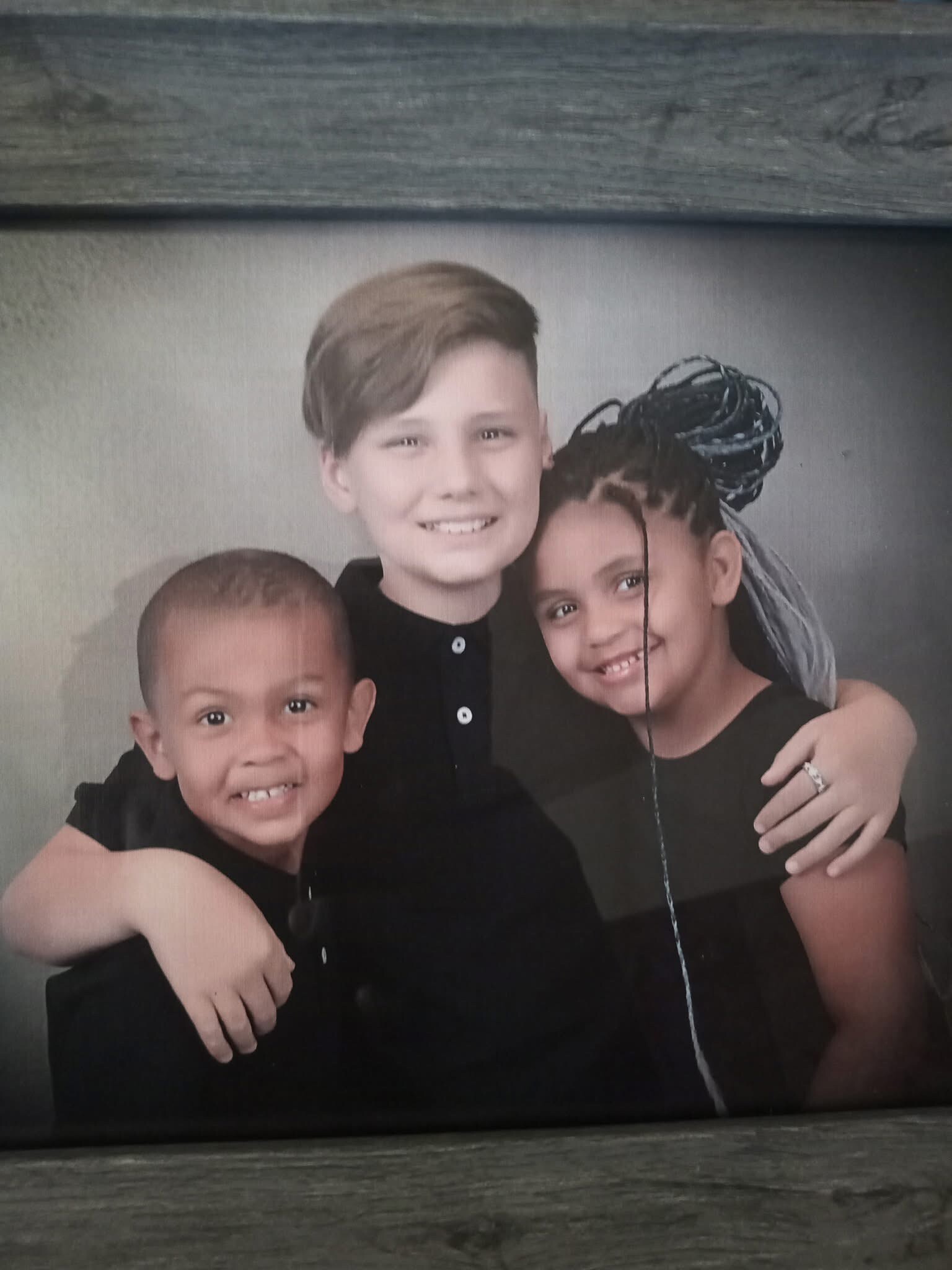 Three children in black shirts pose together, smiling for a studio portrait.