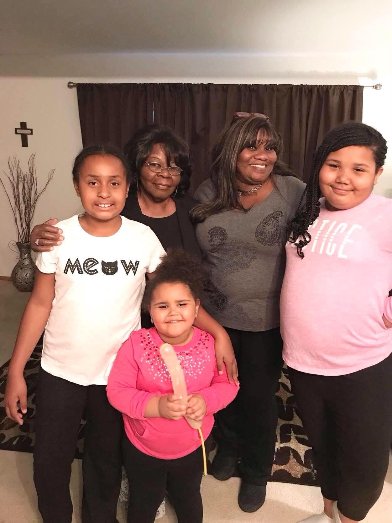 Group of five relatives posing indoors for a photo, two adults in back and three children in front, all smiling at the camera.